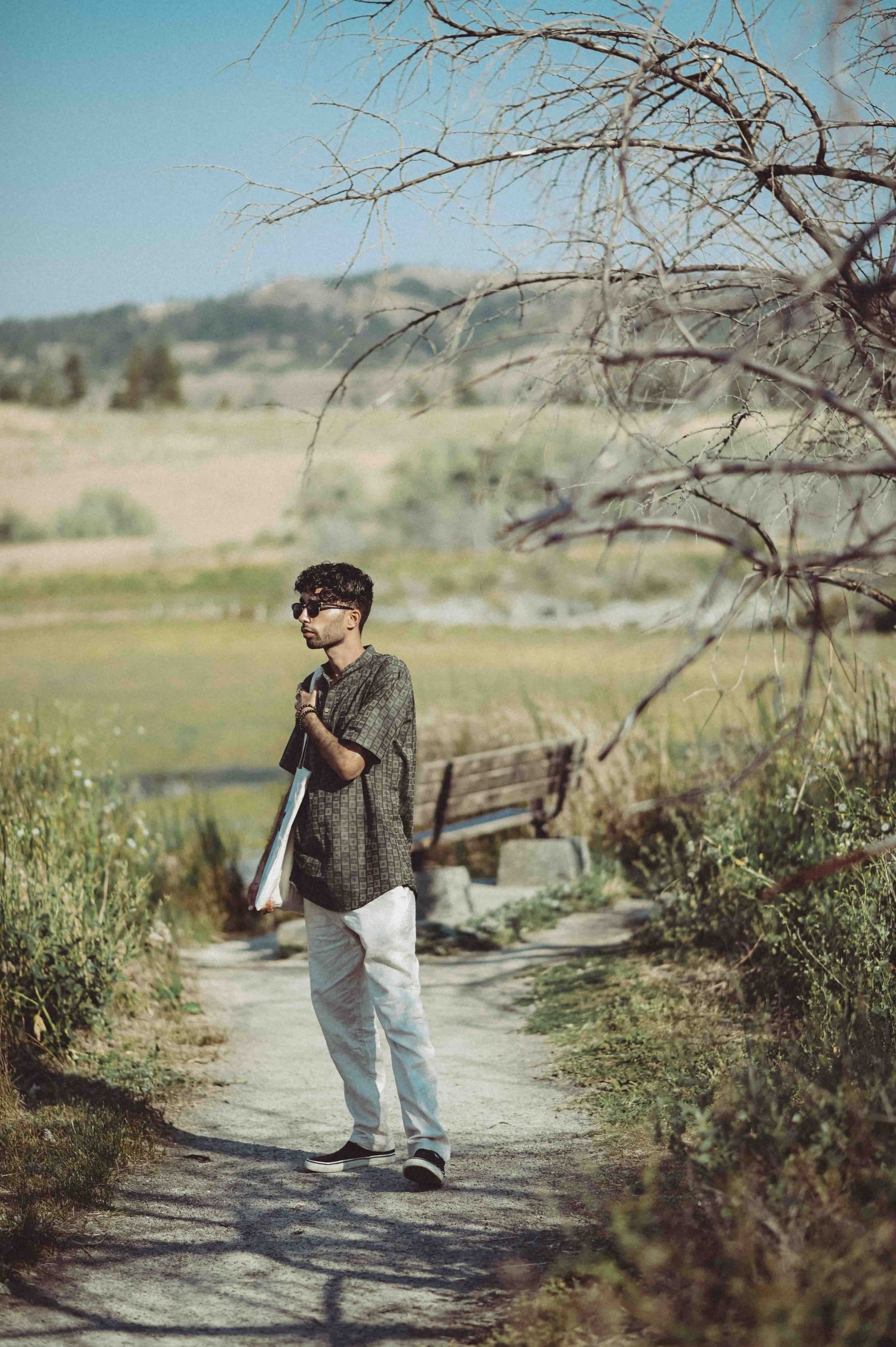 A young man in a patterned shirt and white pants walks along a scenic nature path near a lake.
