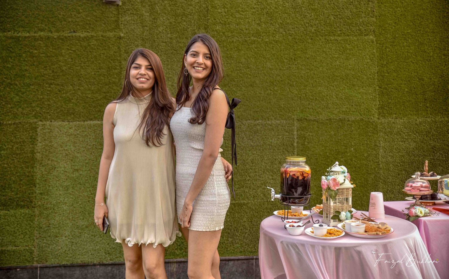 Two women smiling together at a bridal shower dessert table outdoors.