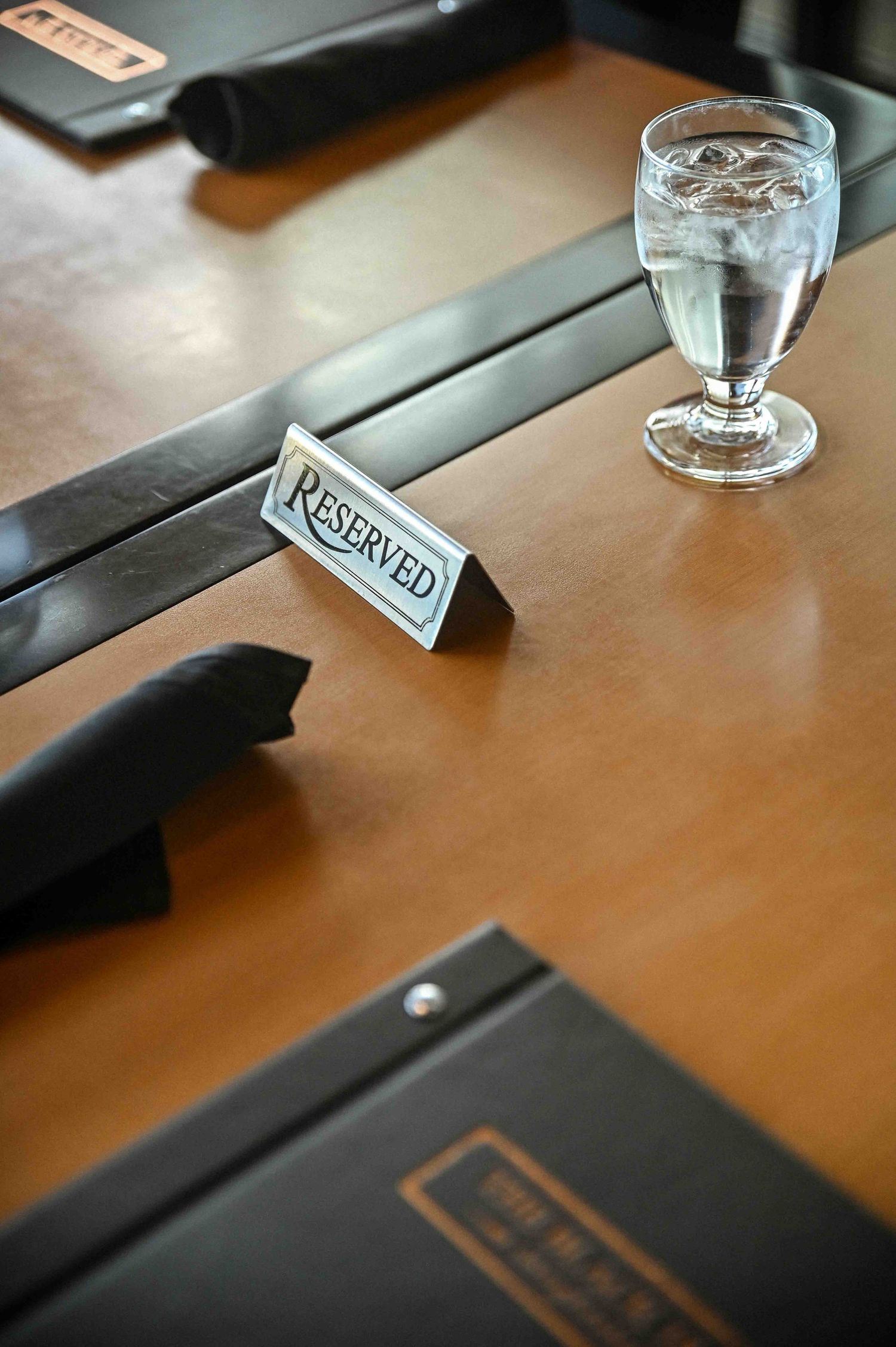 Reserved sign on a restaurant table with water glass and leather menu folders.