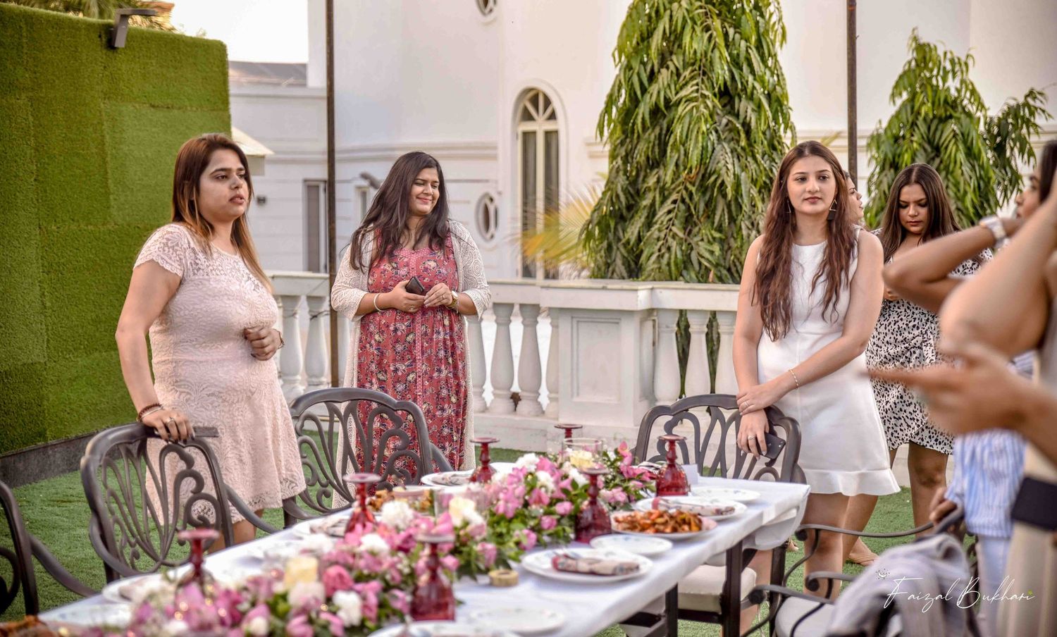 Women socializing at an elegant outdoor garden party with floral table decor.