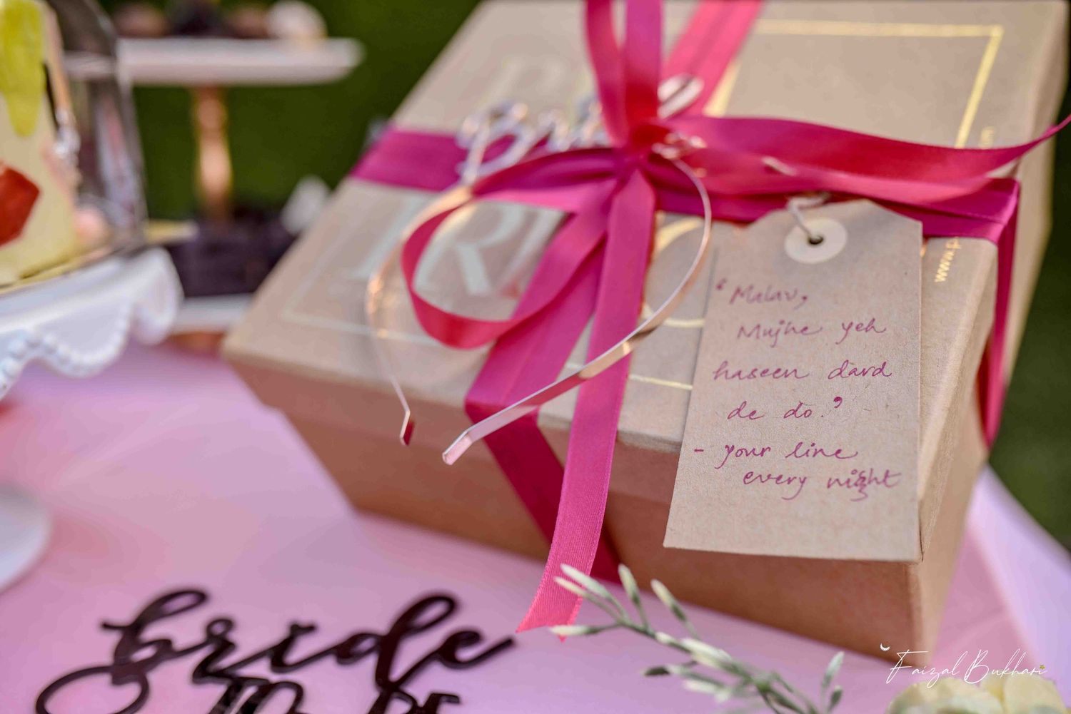 Kraft paper gift box tied with hot pink ribbon and handwritten tag at a bridal shower celebration.