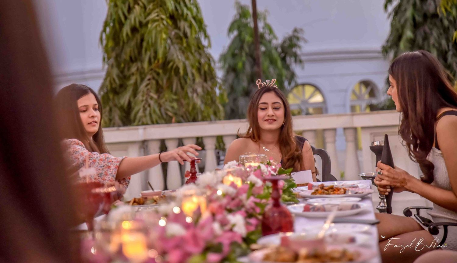 Bride wearing tiara enjoys candlelit outdoor dinner with friends at elegant bridal shower celebration.