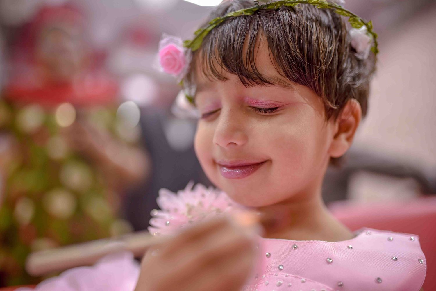 Close-up of a little girl in pink dress with floral crown gently holding a pink feather.
