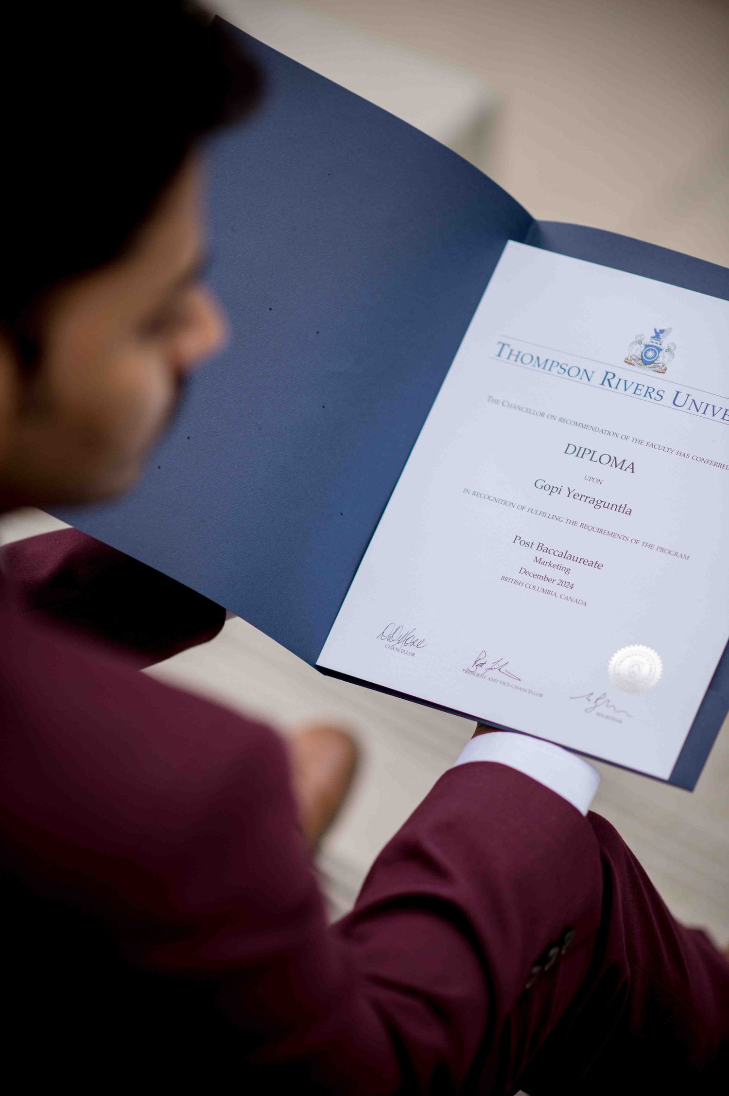 Graduate reviewing Thompson Rivers University diploma in a maroon suit.