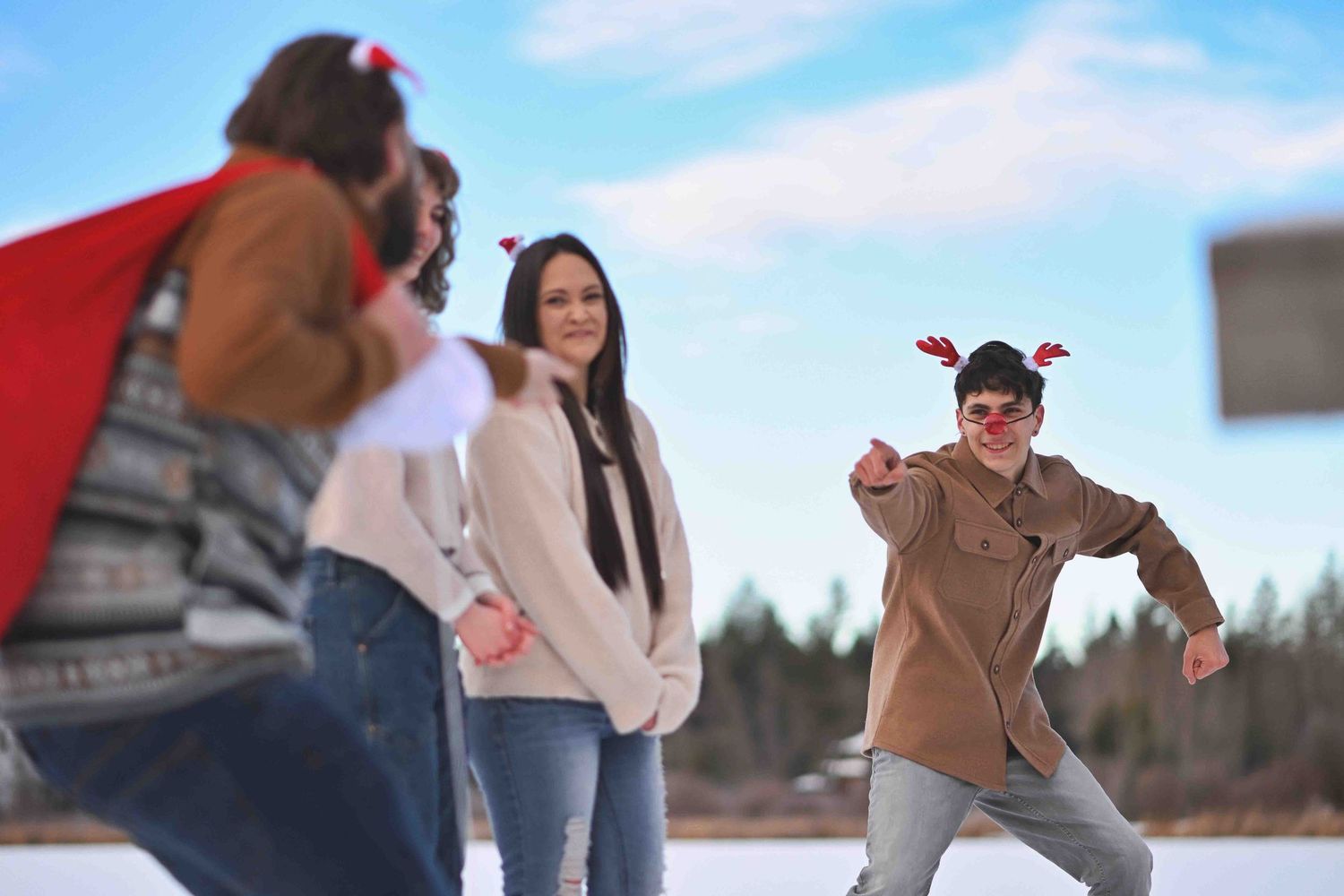 Family enjoying a playful winter outdoor photoshoot near a snowy lake, with one person wearing reindeer antlers.