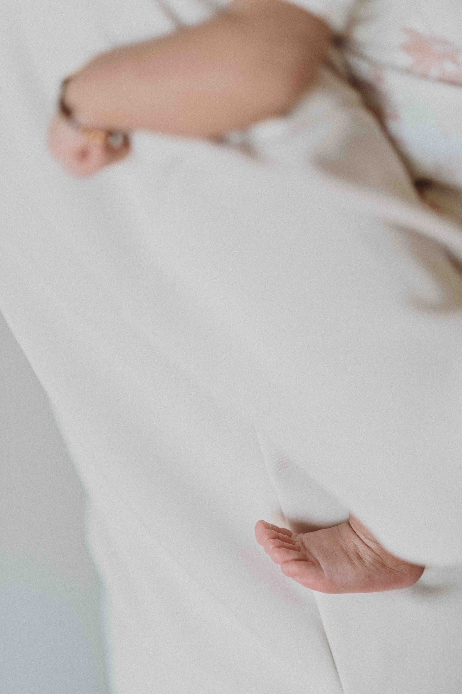 Close-up of pregnant woman in white dress showing baby bump with delicate hand detail and bracelet.