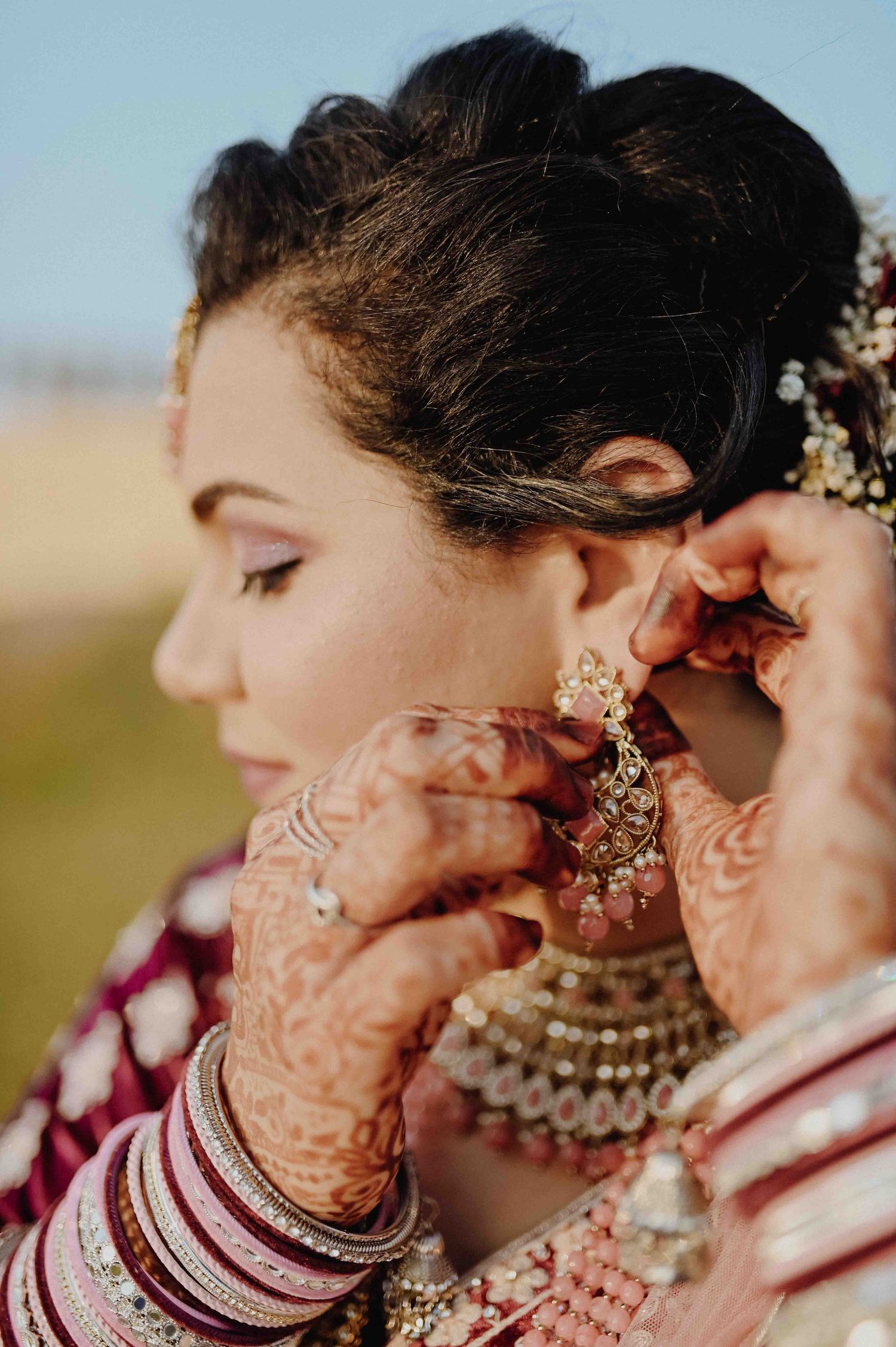 Bride having ornate kundan earring adjusted, hands adorned with mehndi and bangles.