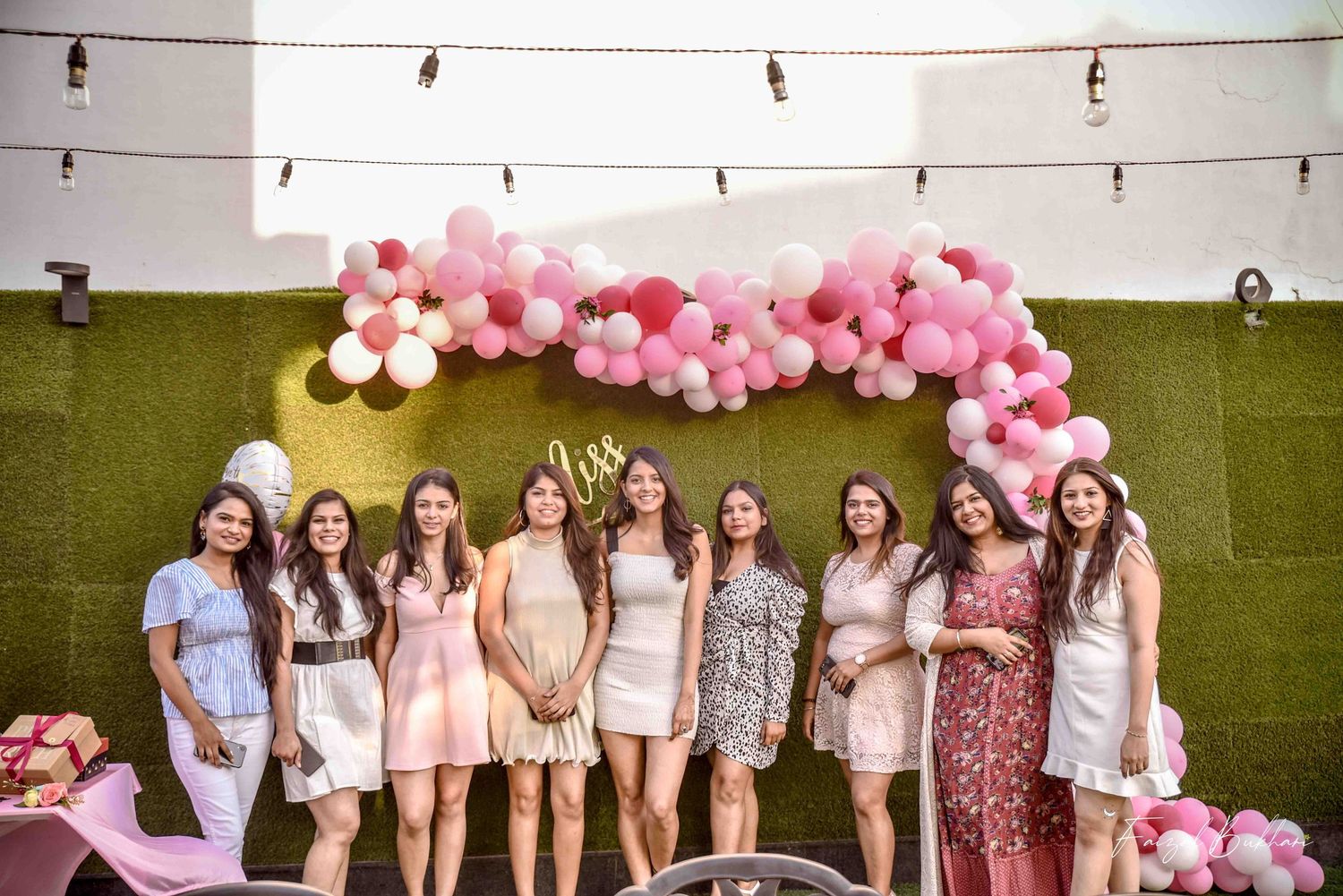 Group of women posing in front of a pink and white balloon arch at an outdoor bridal shower.