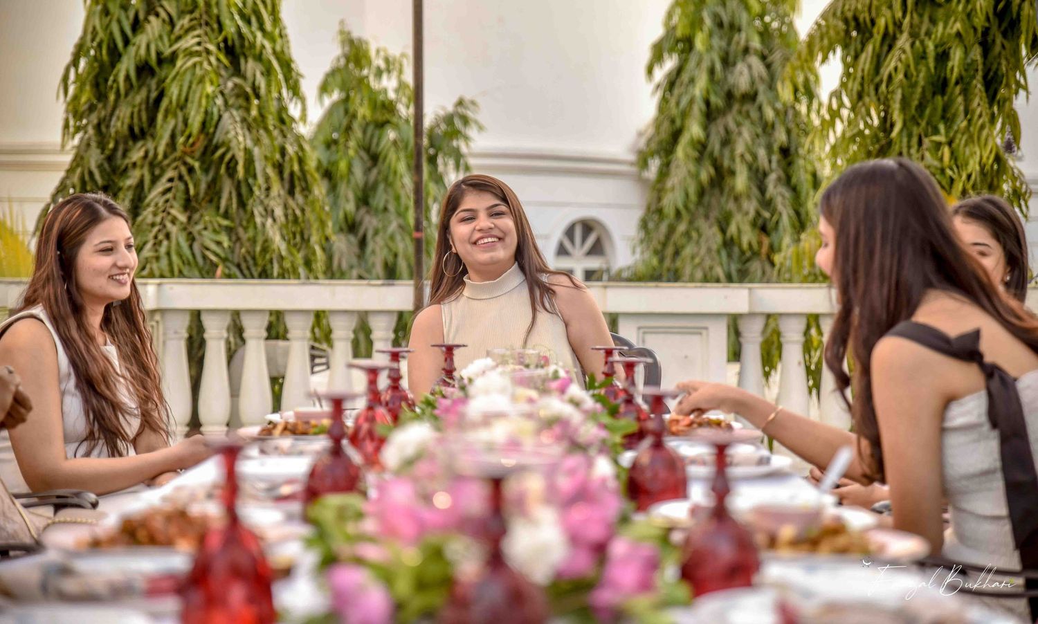 Women laughing and dining at an elegant outdoor floral garden party table.
