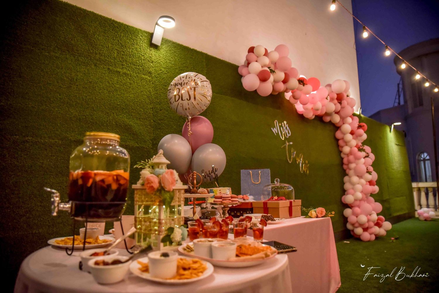 Elegant Miss to Mrs bridal shower dessert table with pink balloon arch, drinks dispenser and string lights.