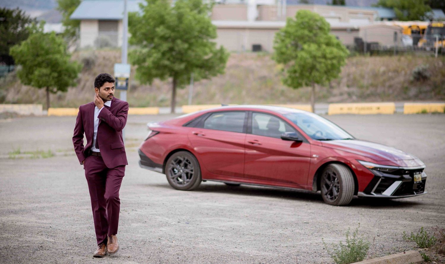 Stylish man in maroon suit standing beside a matching red sports car in a parking lot.