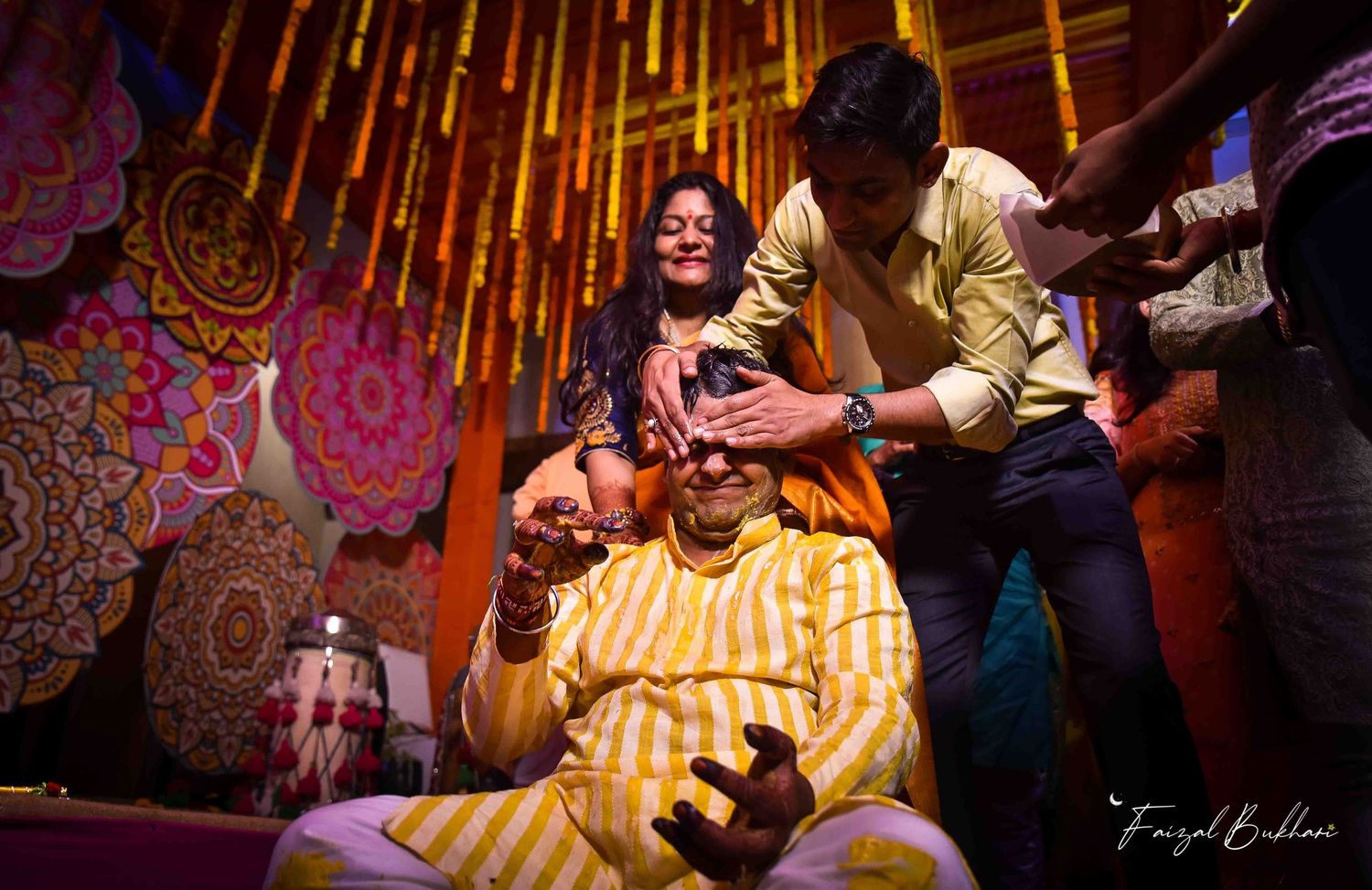 Family members applying haldi paste on groom during traditional Indian pre-wedding haldi ceremony.