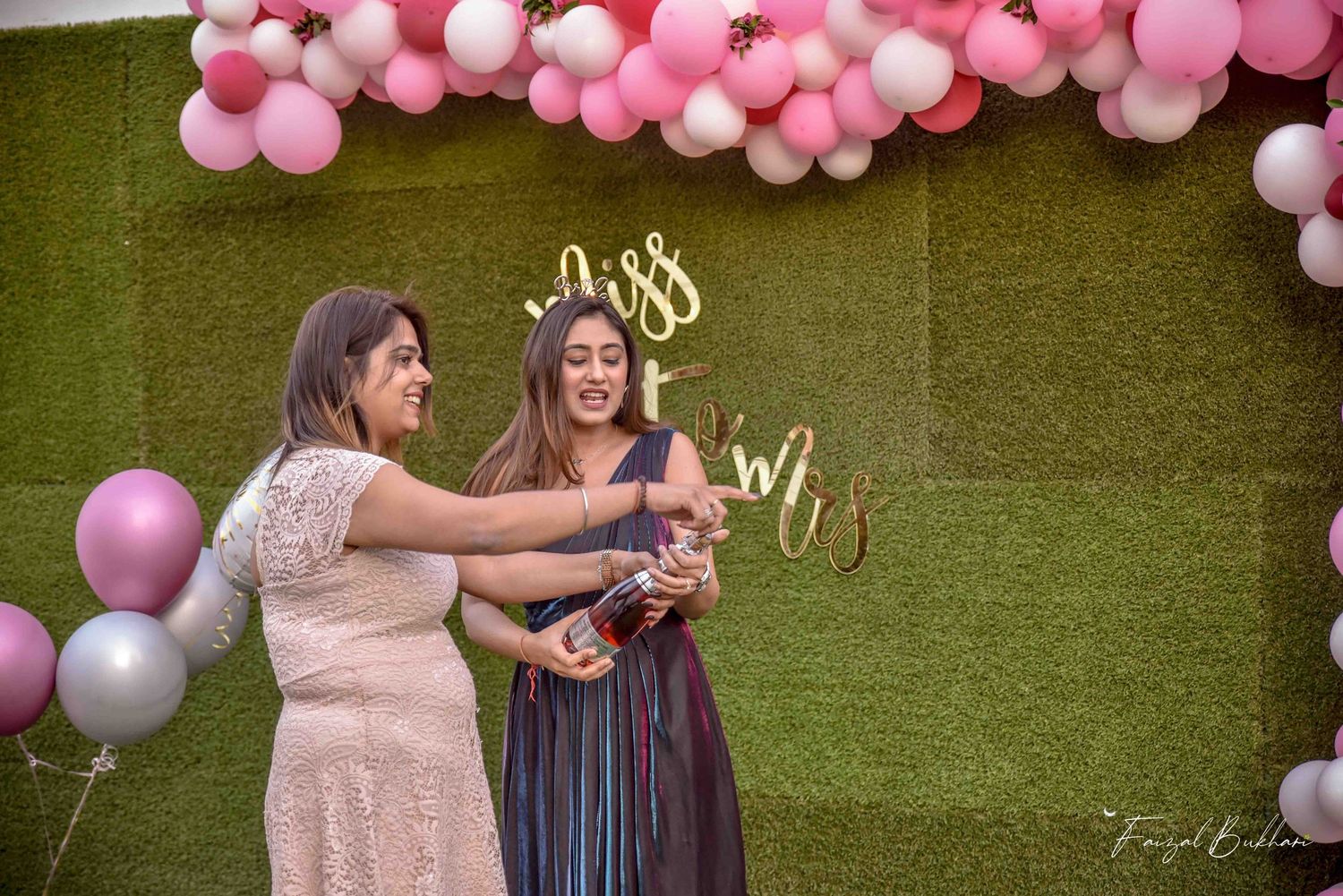 Two women popping champagne together at a pink balloon Miss to Mrs bridal shower.