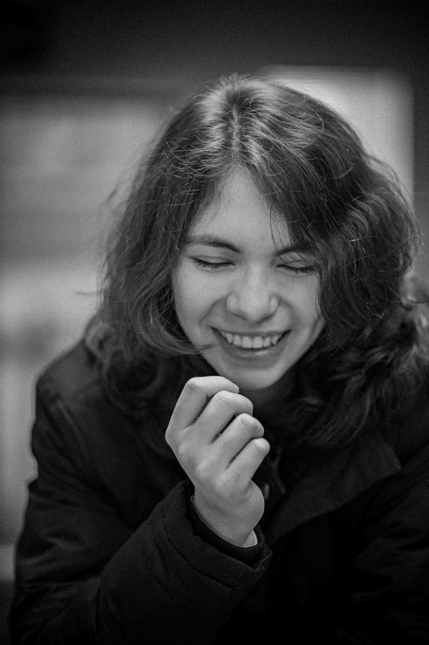 A young person with long hair laughs joyfully in a black-and-white portrait photo.