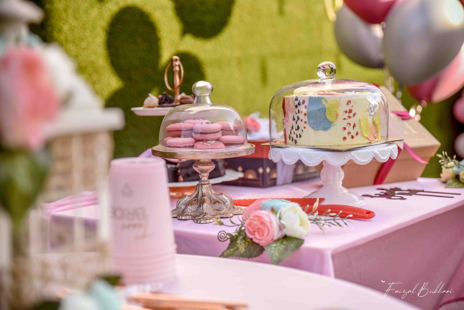 Pink bridal shower dessert table featuring macarons, decorated cake, and elegant silver cake stands.