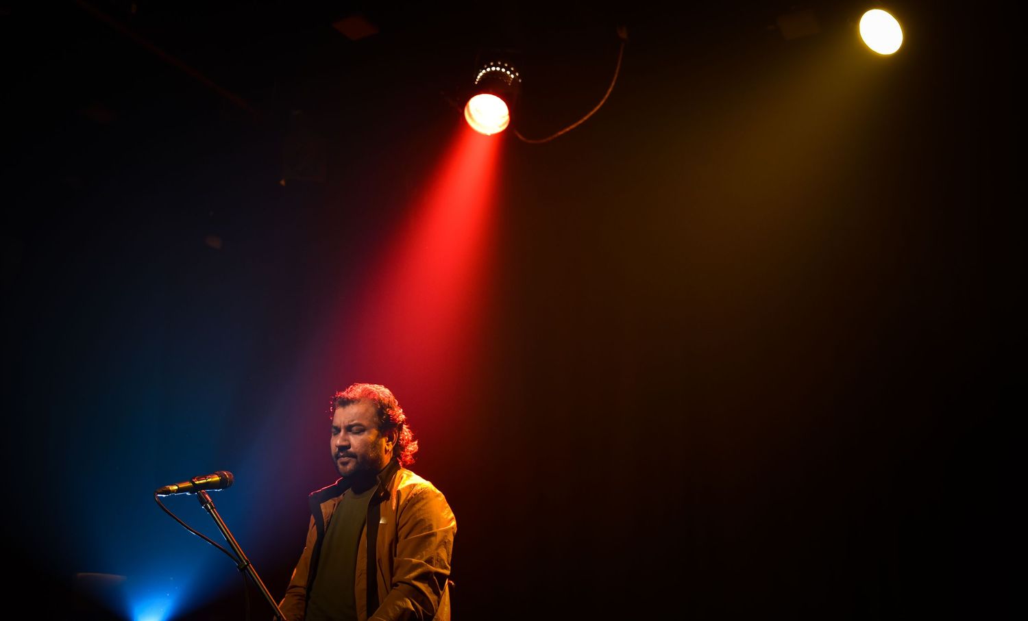 Male singer performing on stage under red and yellow spotlights in a darkened concert venue.
