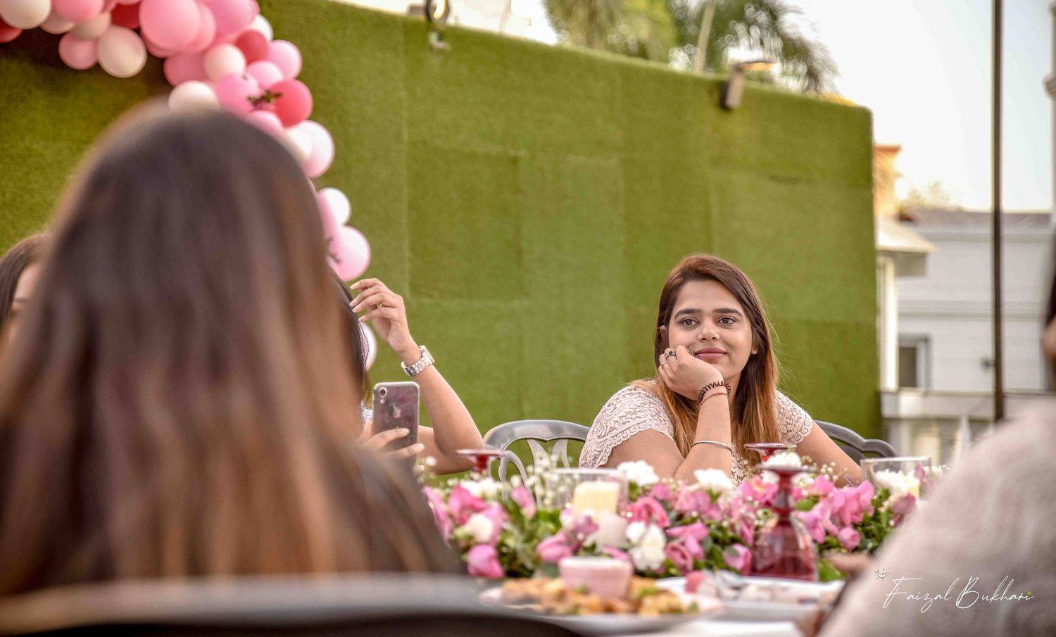 Happy woman resting chin on hand at pink balloon-decorated outdoor bridal party table.