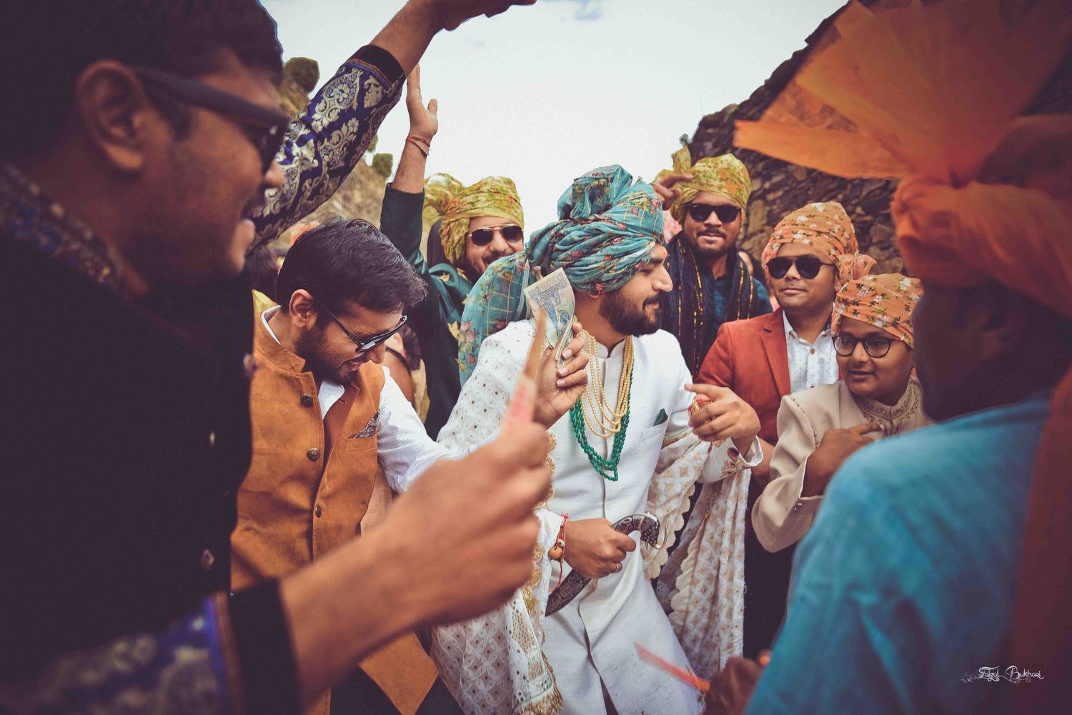 Groom in teal turban and white sherwani celebrates with friends during a vibrant Indian wedding baraat procession.