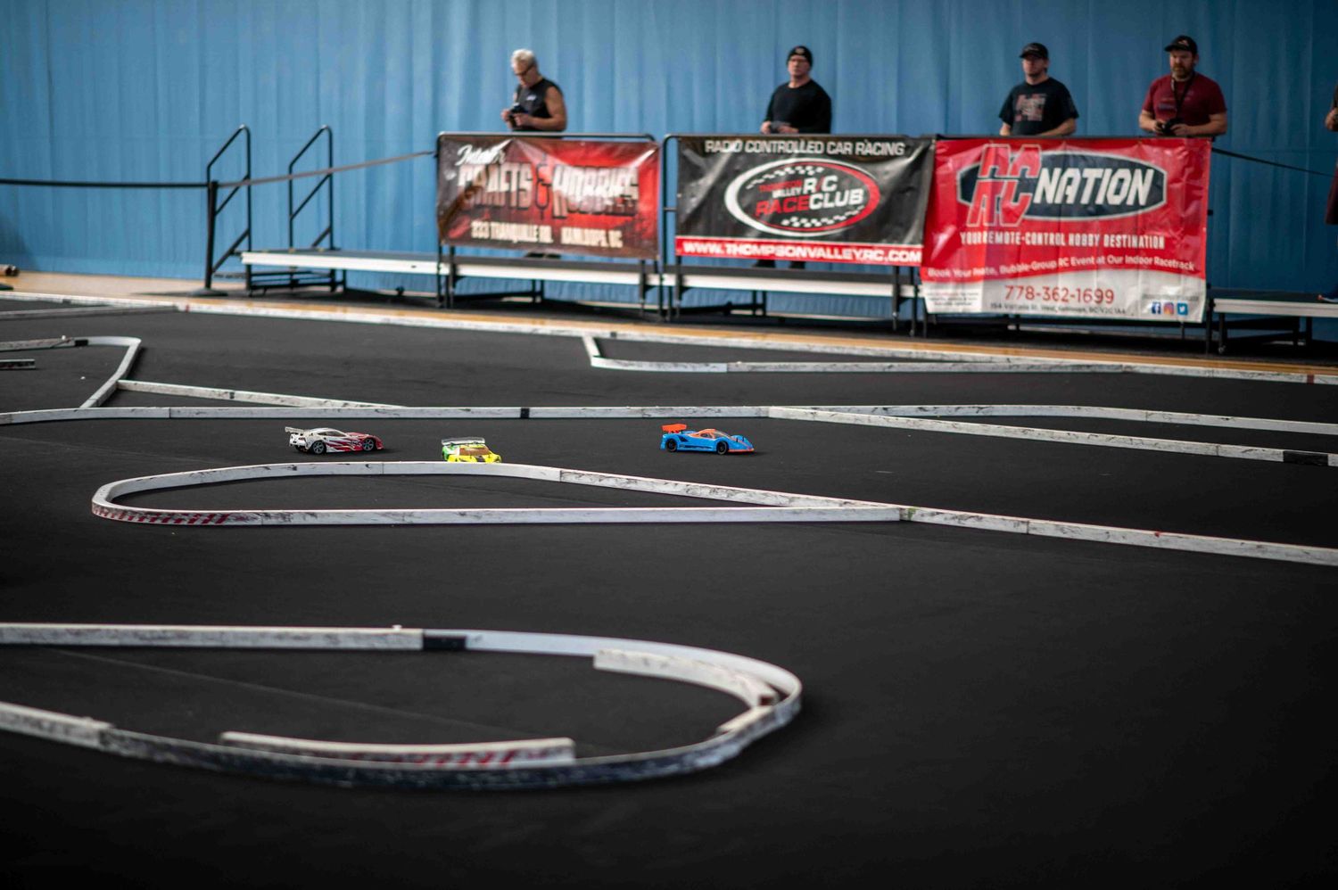 Aerial view of an indoor RC car racing track with sponsor banners and spectators.