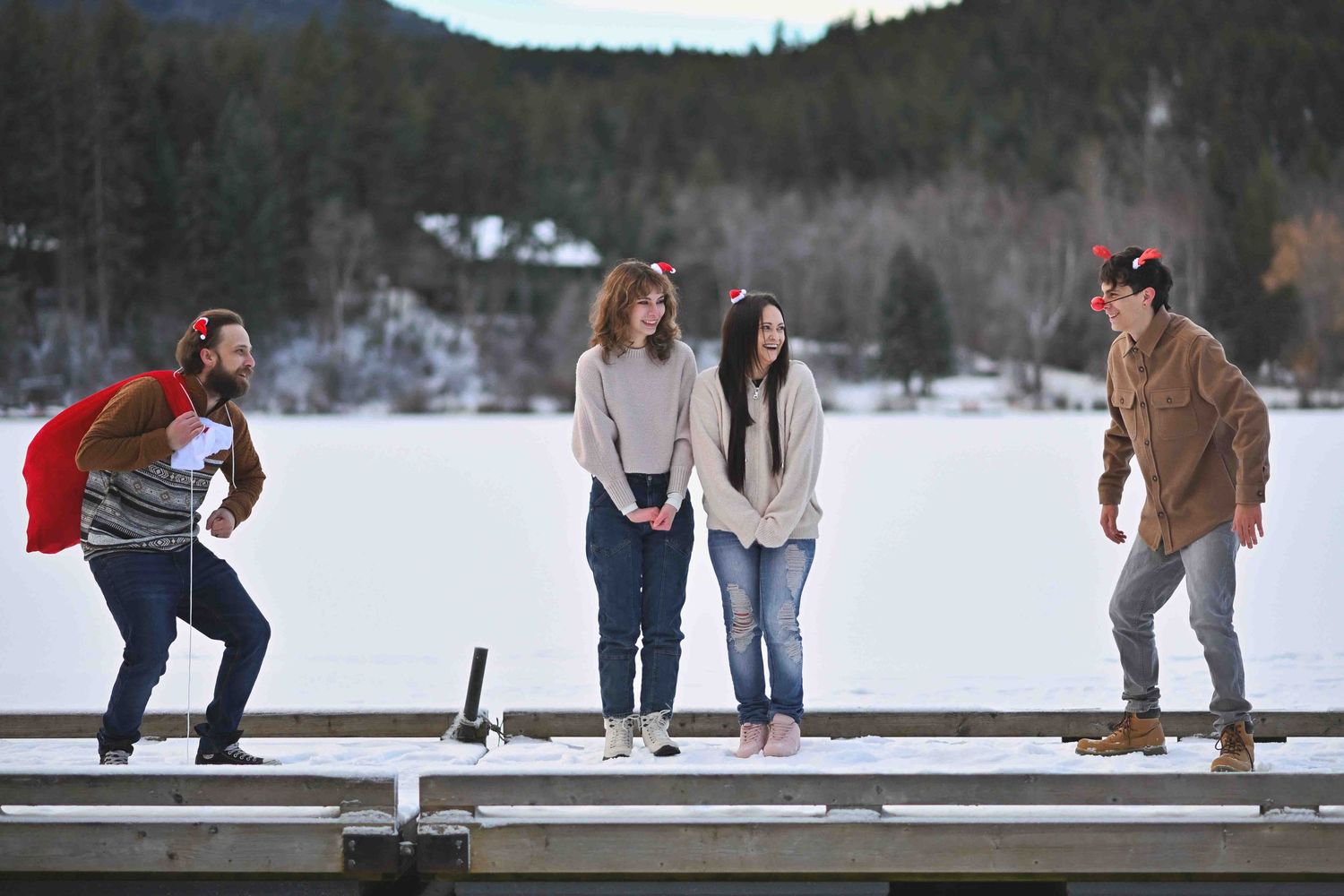 Four family members standing on a snowy dock in winter, posing playfully near a frozen lake surrounded by trees.
