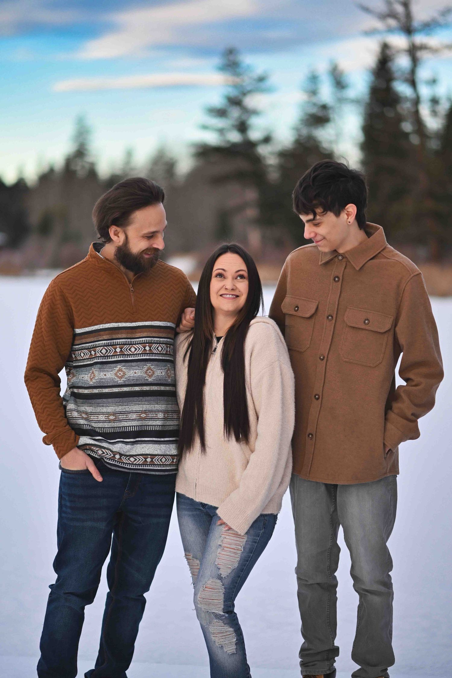 Three Family members smiling warmly together outdoors on a frozen snowy landscape during a winter photo session.