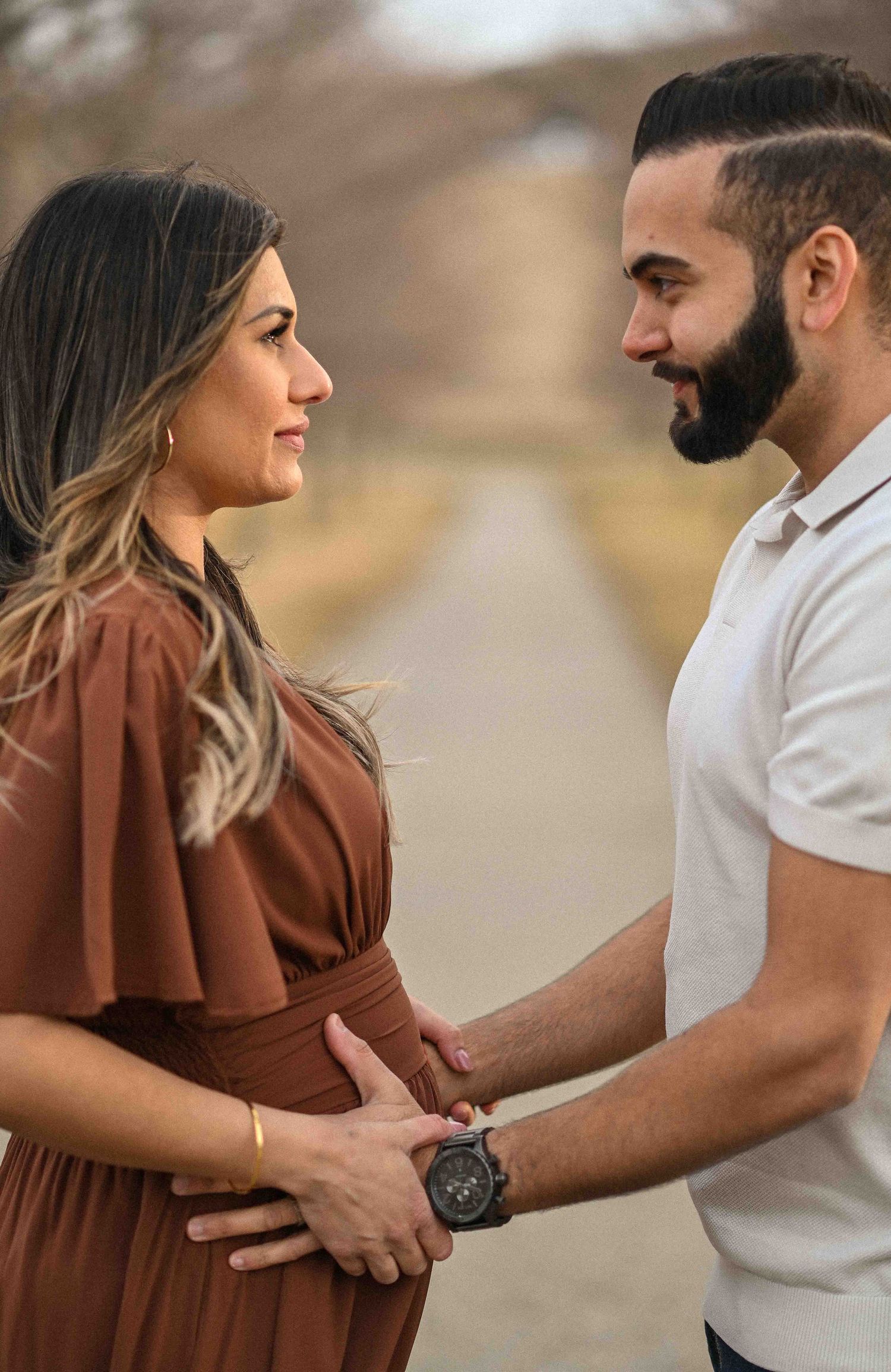 Expecting couple holding hands and smiling at each other during maternity photoshoot.