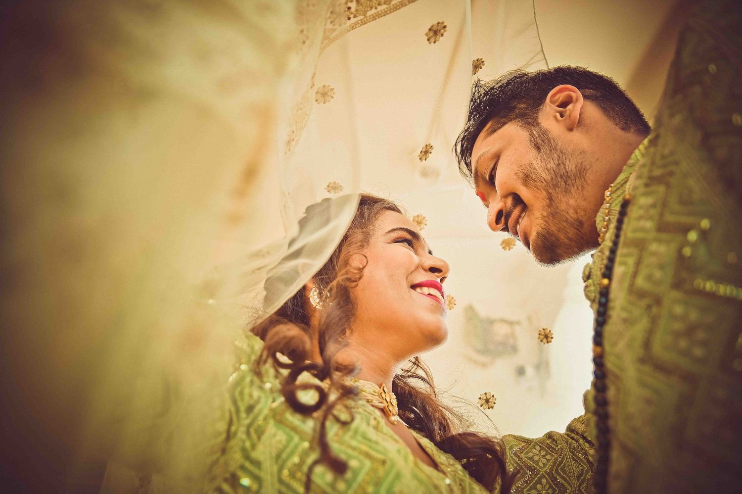 An Indian bride and groom in green traditional attire sharing a loving glance at their wedding.