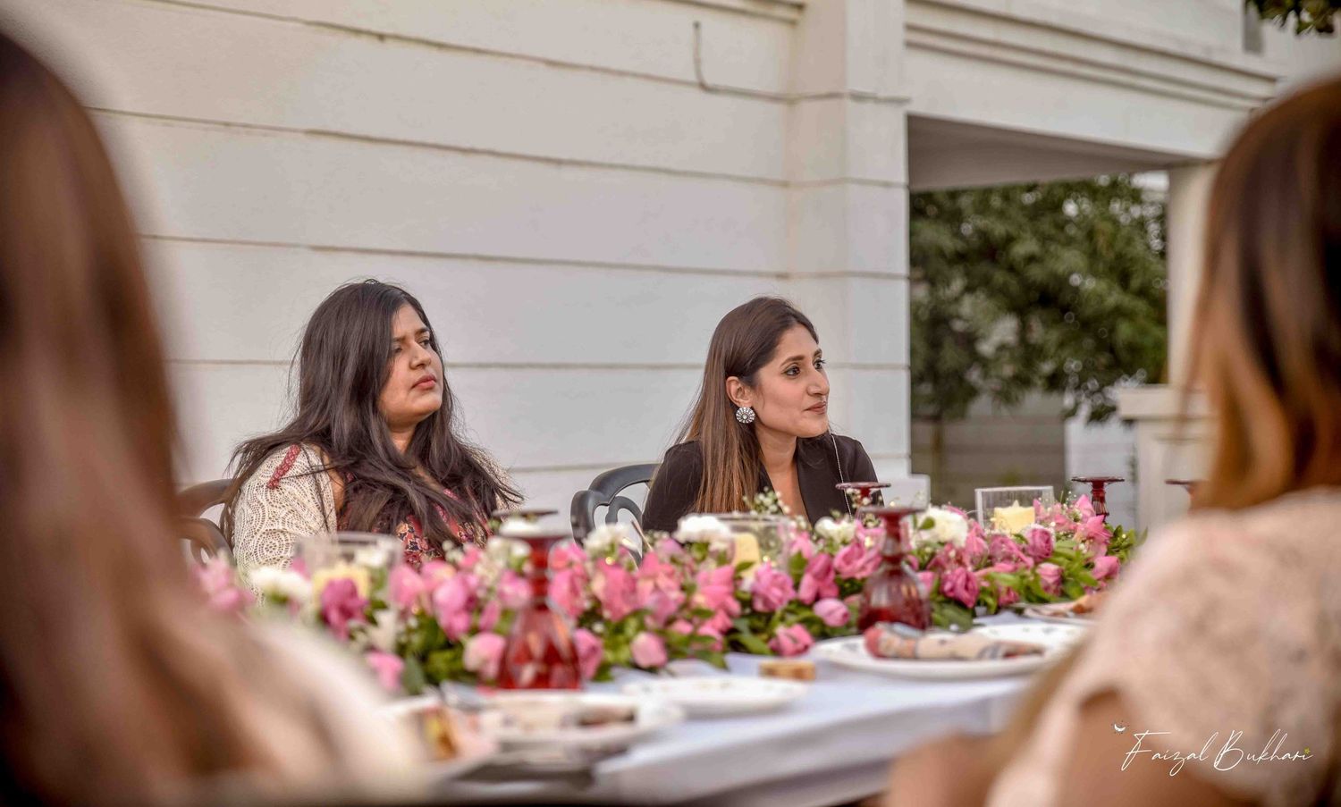 Two women sitting at a floral decorated table at an outdoor garden party.