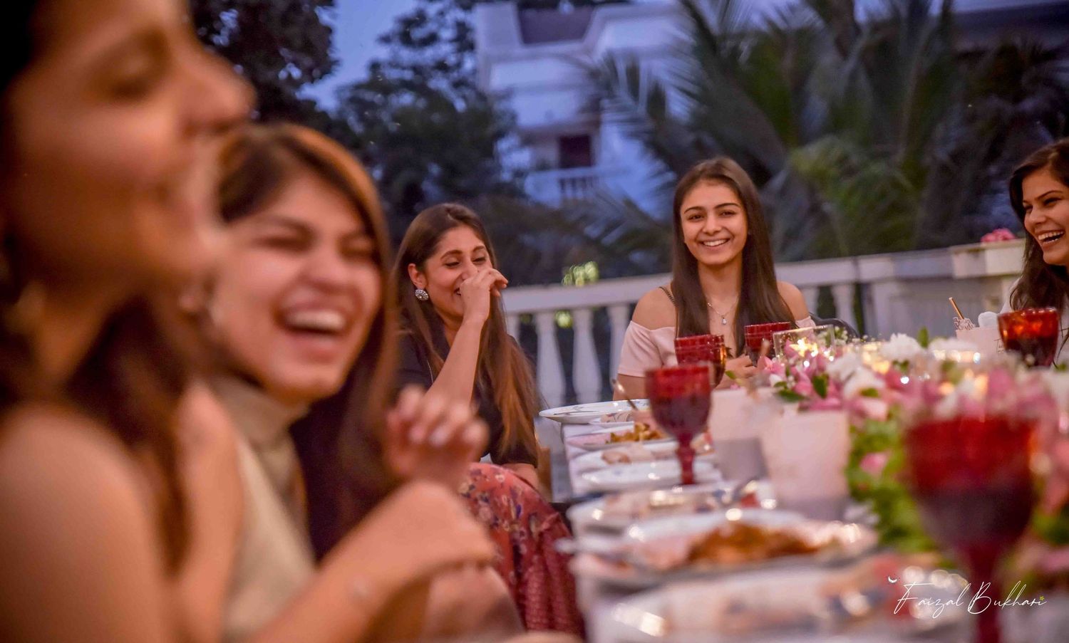 Group of women laughing and celebrating together at a candlelit outdoor bridal shower dinner party.