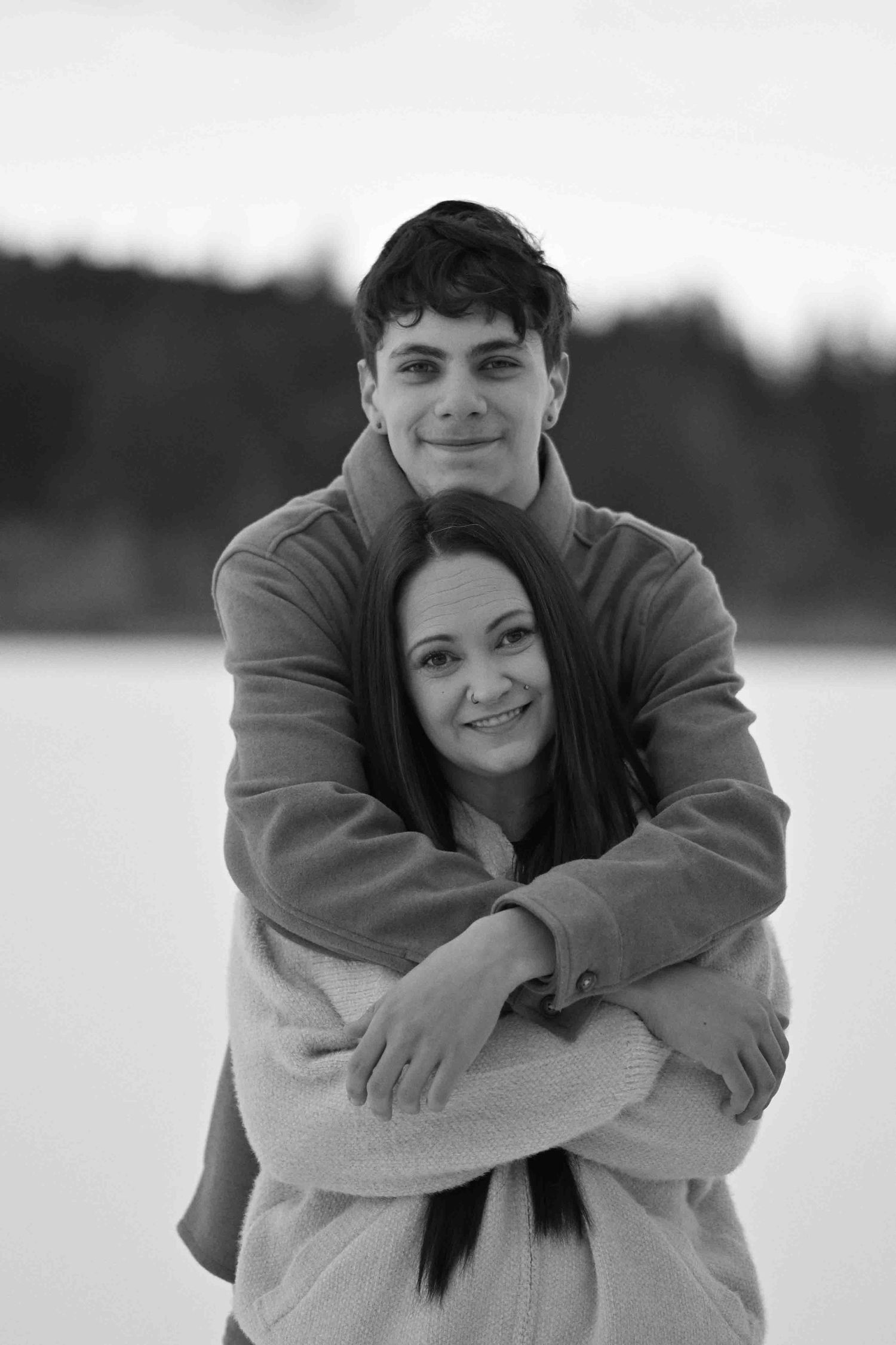 Black and white portrait of young couple embracing warmly in a snowy winter outdoor setting.