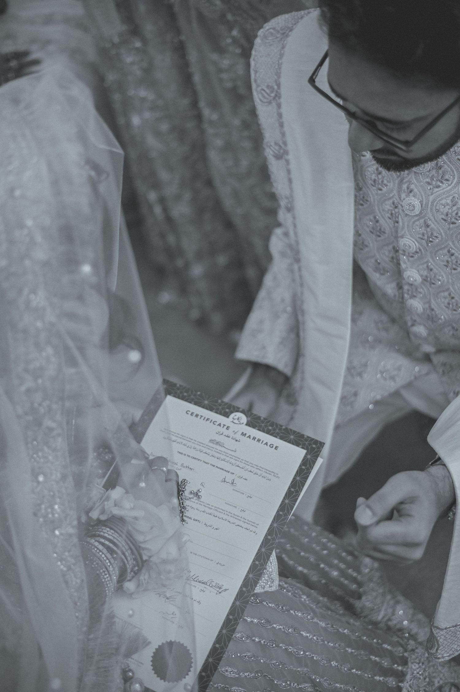 Couple signing a Certificate of Marriage document in black and white wedding photo.