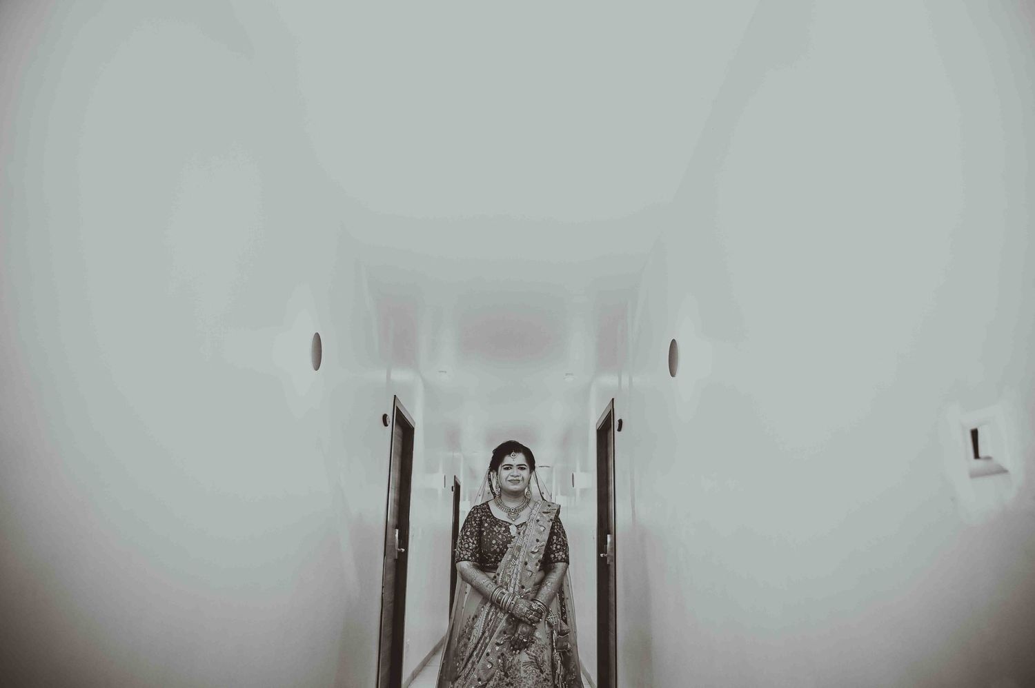 A bride in traditional Indian attire walks gracefully down a white hallway in this artistic black and white wedding photo.