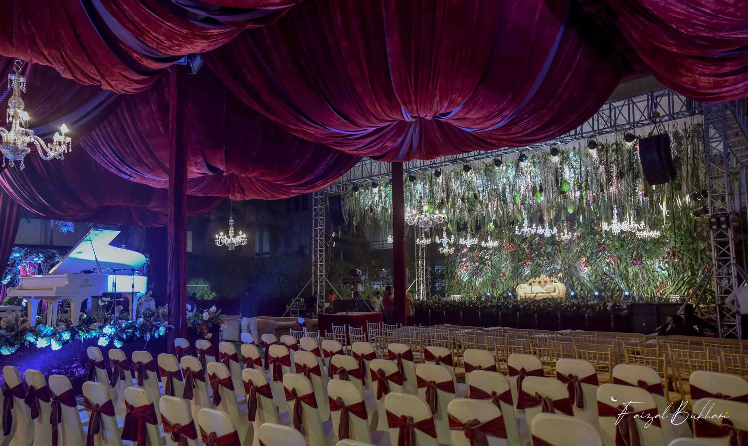 Elegant Indian wedding venue decorated with purple drapes, chandeliers and floral backdrop with white chairs.