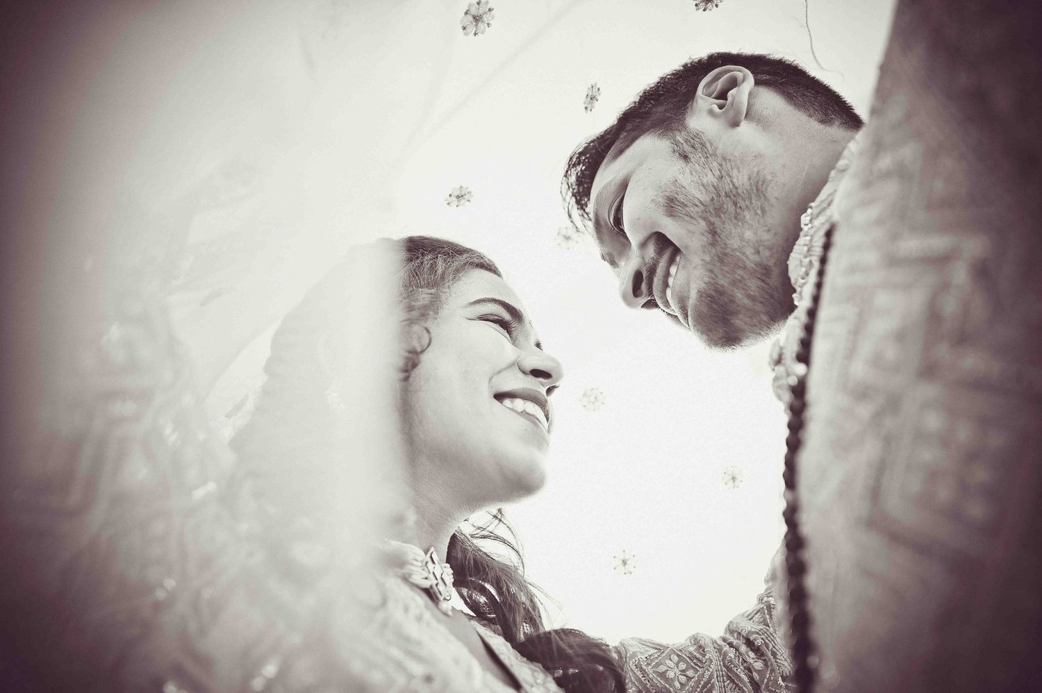 Black and white intimate portrait of smiling Indian bride and groom sharing a tender wedding moment.