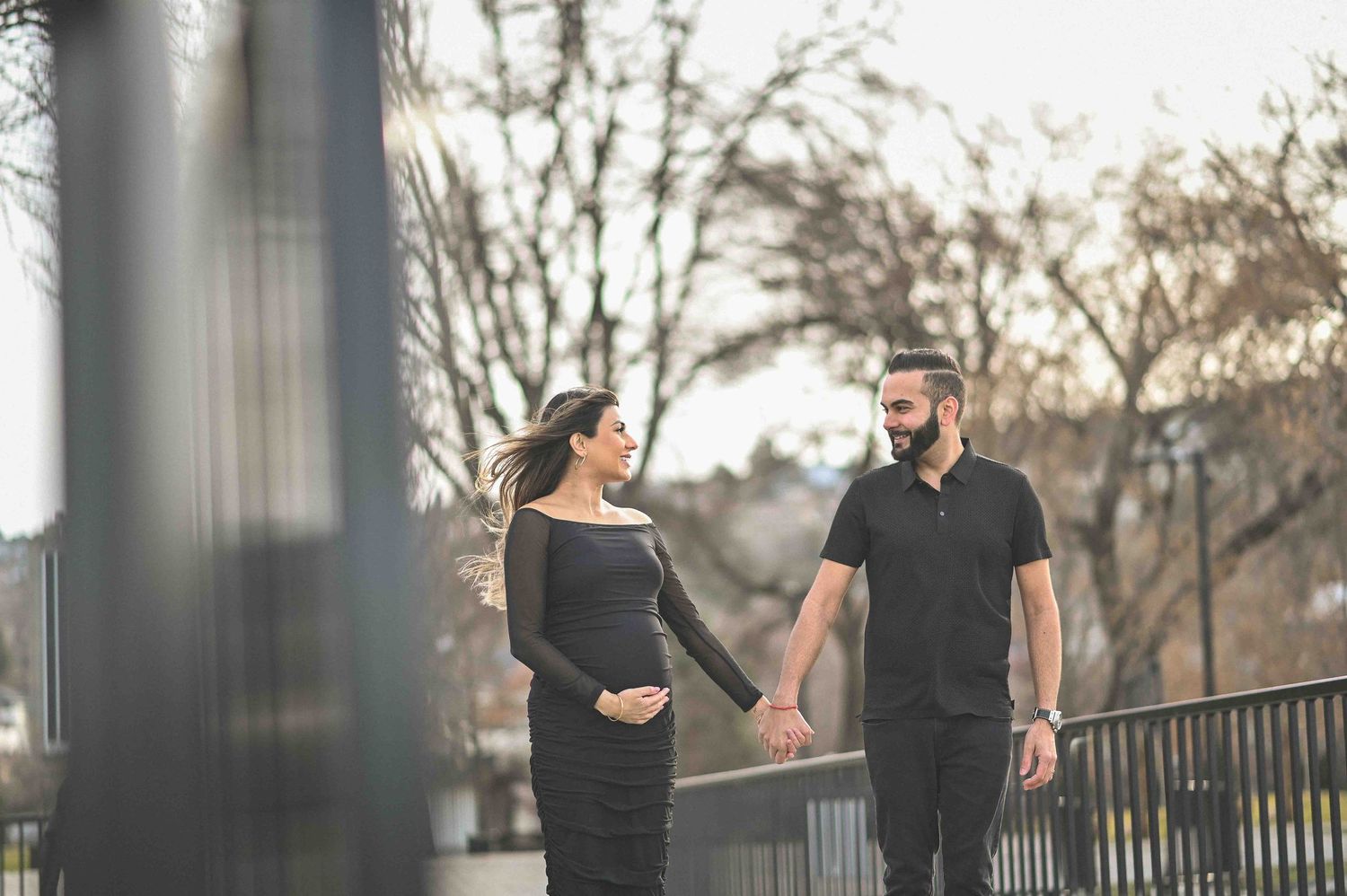 Pregnant couple strolling on a bridge, holding hands during outdoor maternity session.