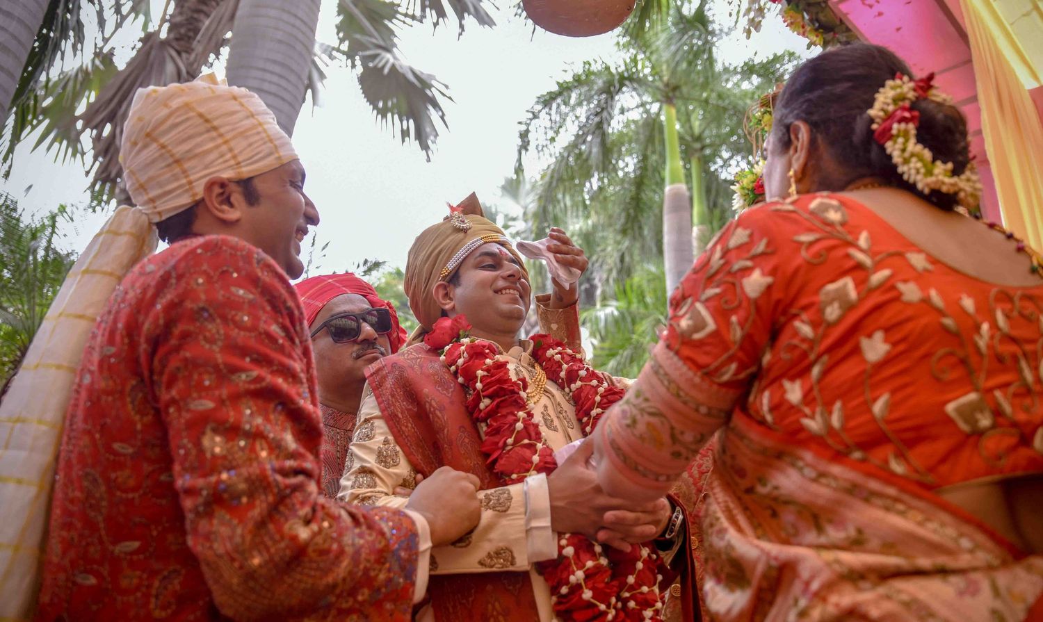 An Indian groom in red sherwani and turban sharing a warm moment with family at his wedding.