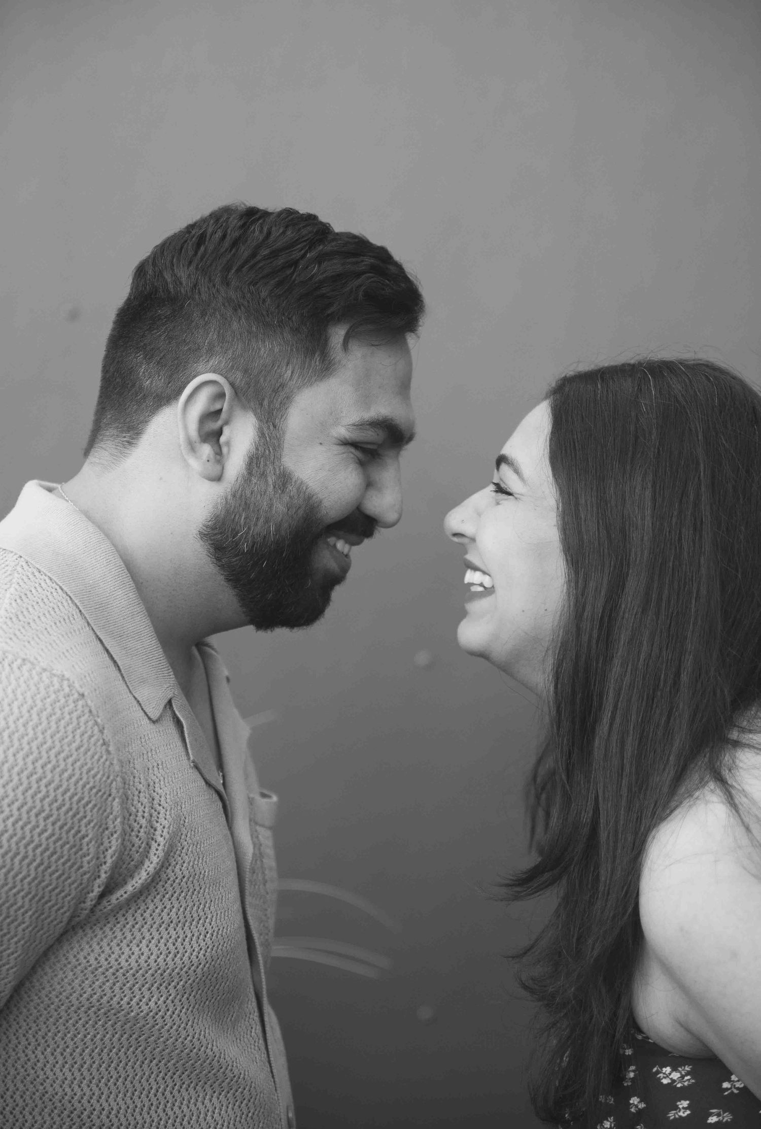 Black and white close-up of a smiling couple facing each other, sharing a joyful intimate moment.