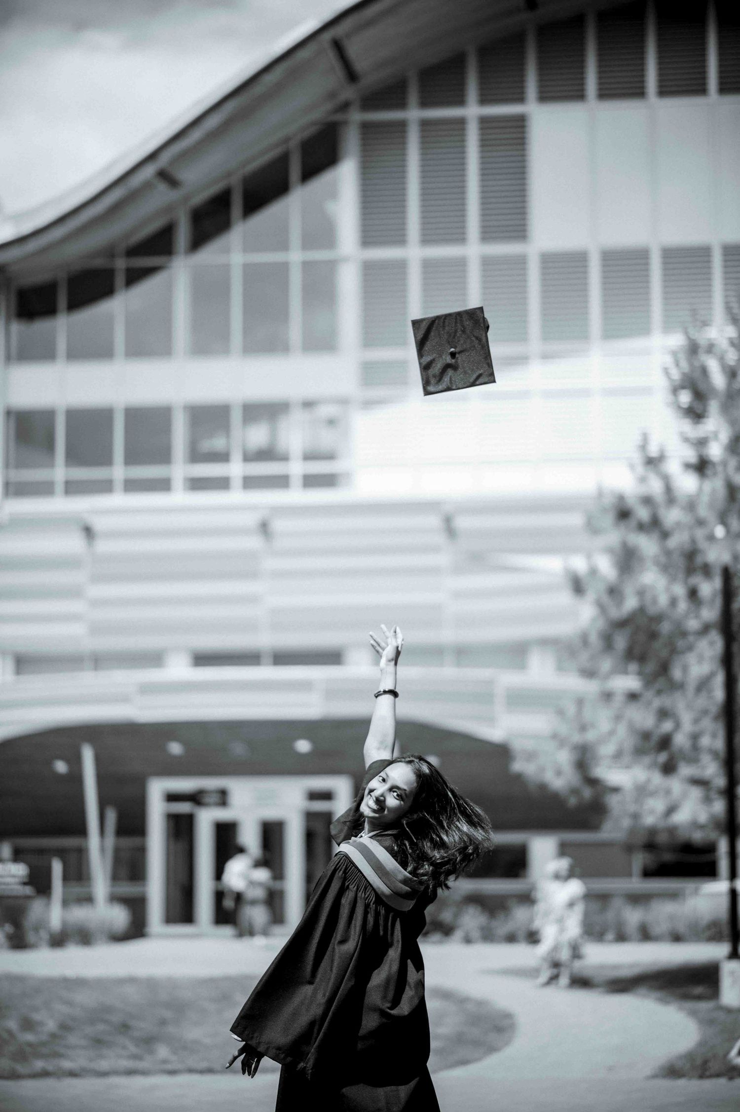 Black and white photo of a graduate in cap and gown tossing mortarboard in the air.