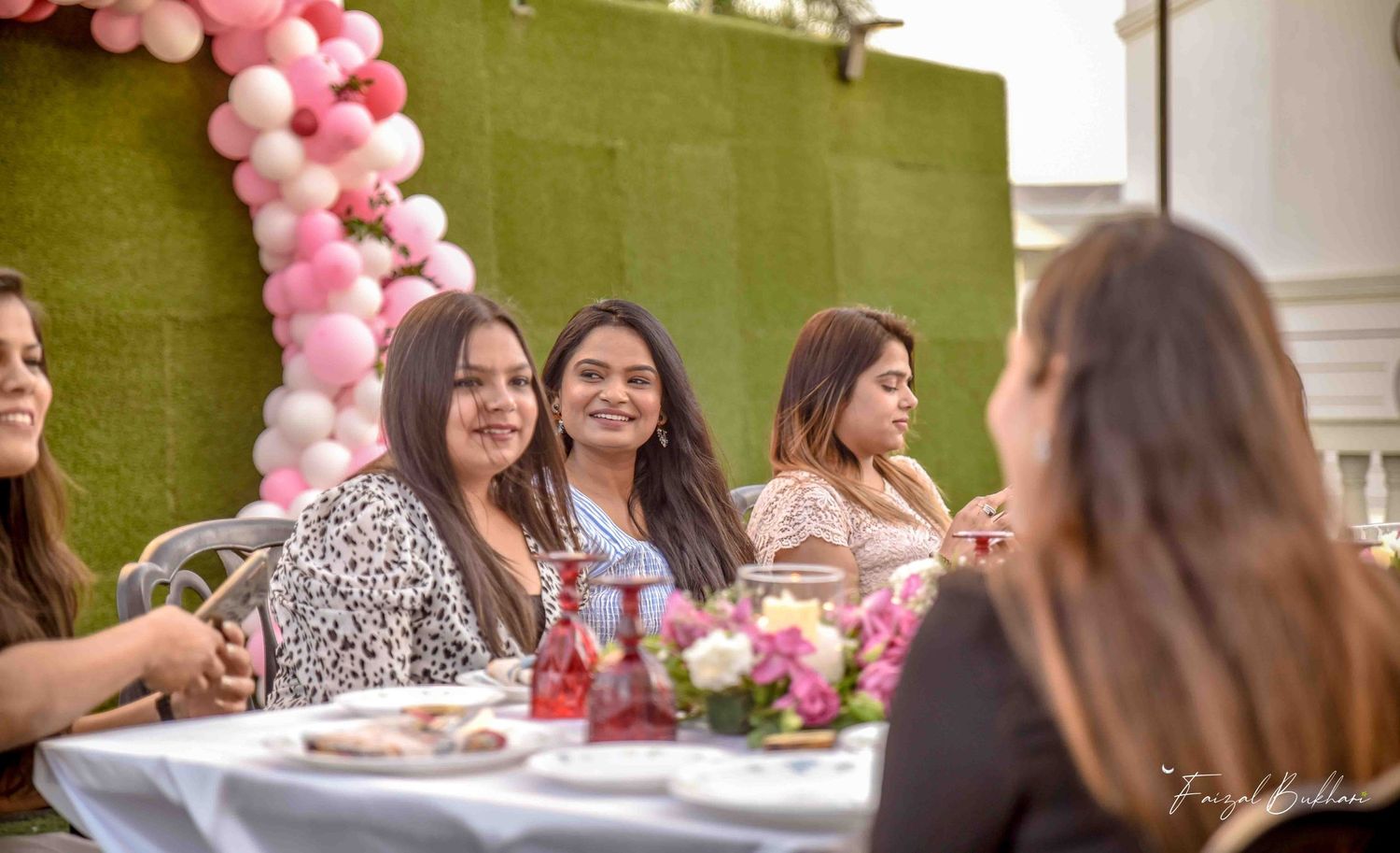 Women smiling at outdoor bridal shower with pink balloon arch.