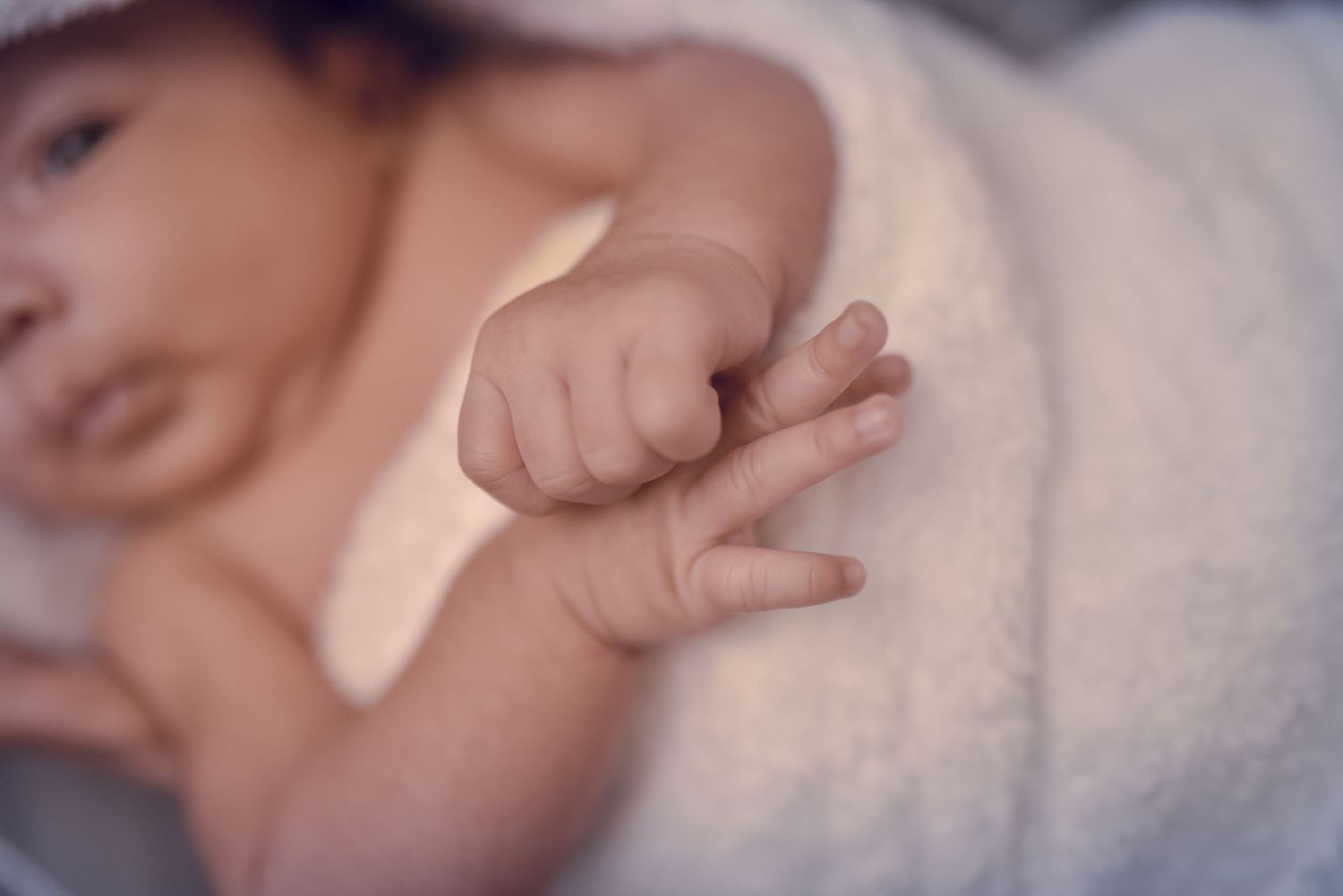 Close-up of a newborn baby's tiny hand and fingers resting on a soft white towel.
