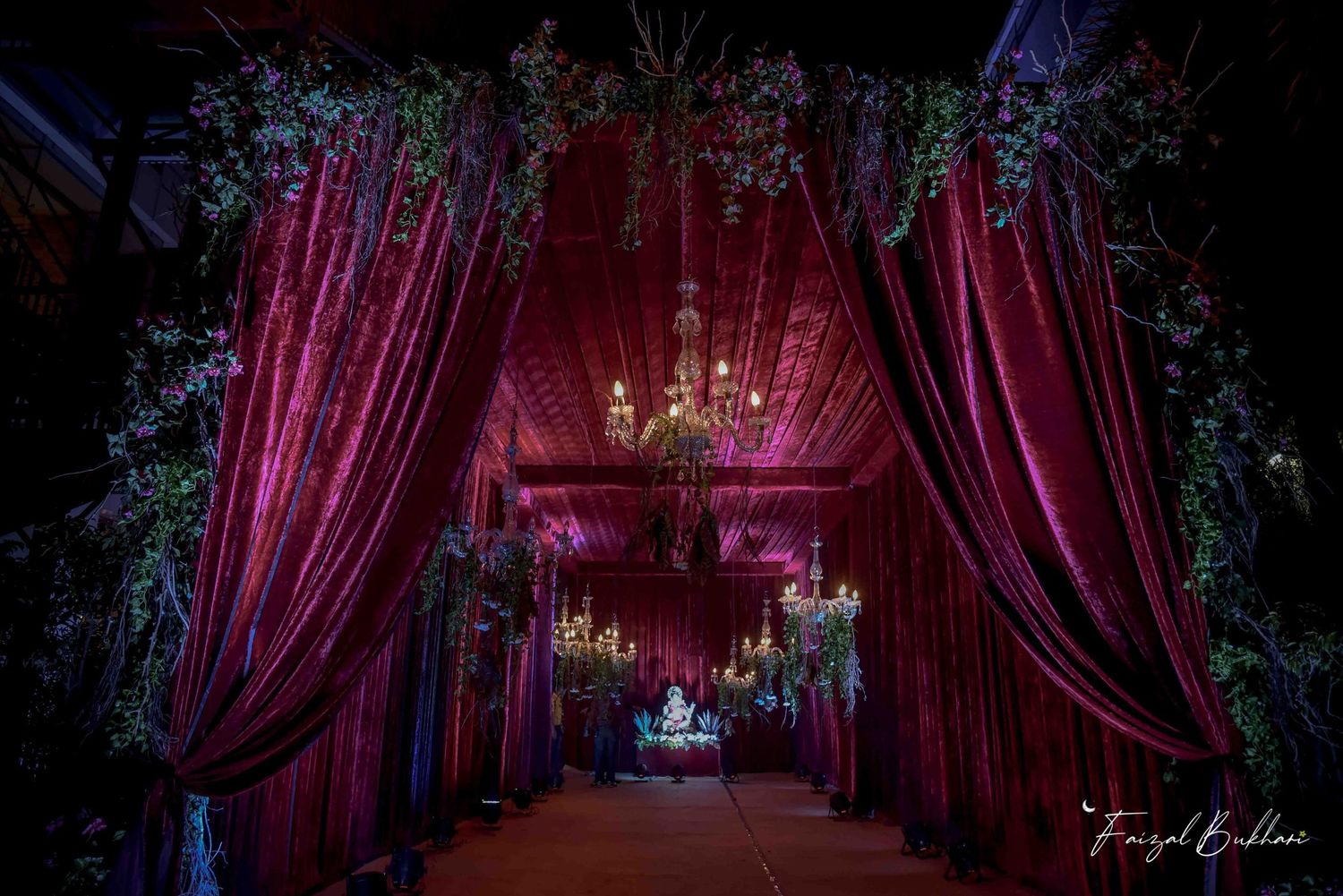 Elegant wedding entrance draped in rich burgundy velvet curtains with chandelier lighting and floral decor.
