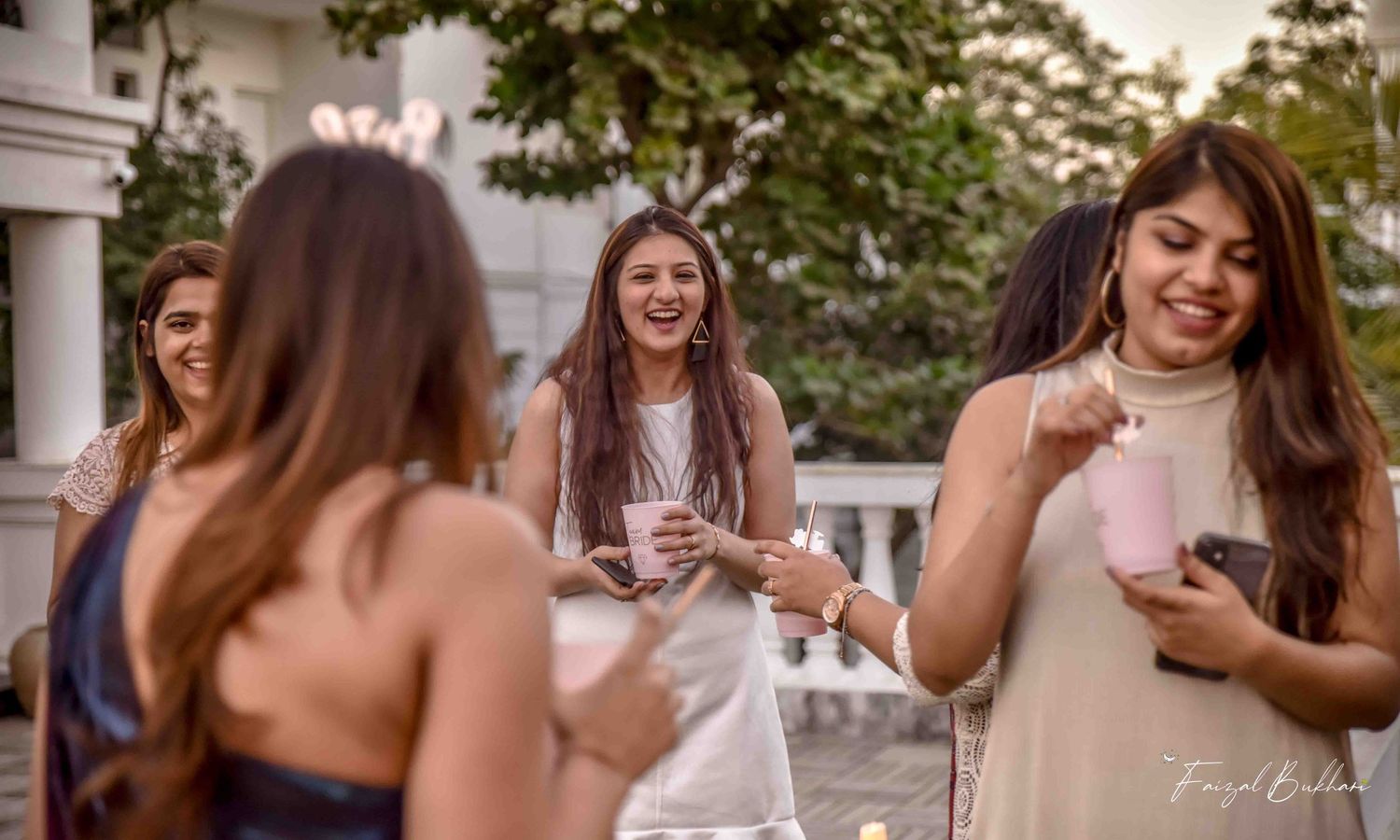 Three women laughing and enjoying drinks together at an elegant outdoor bridal shower celebration.