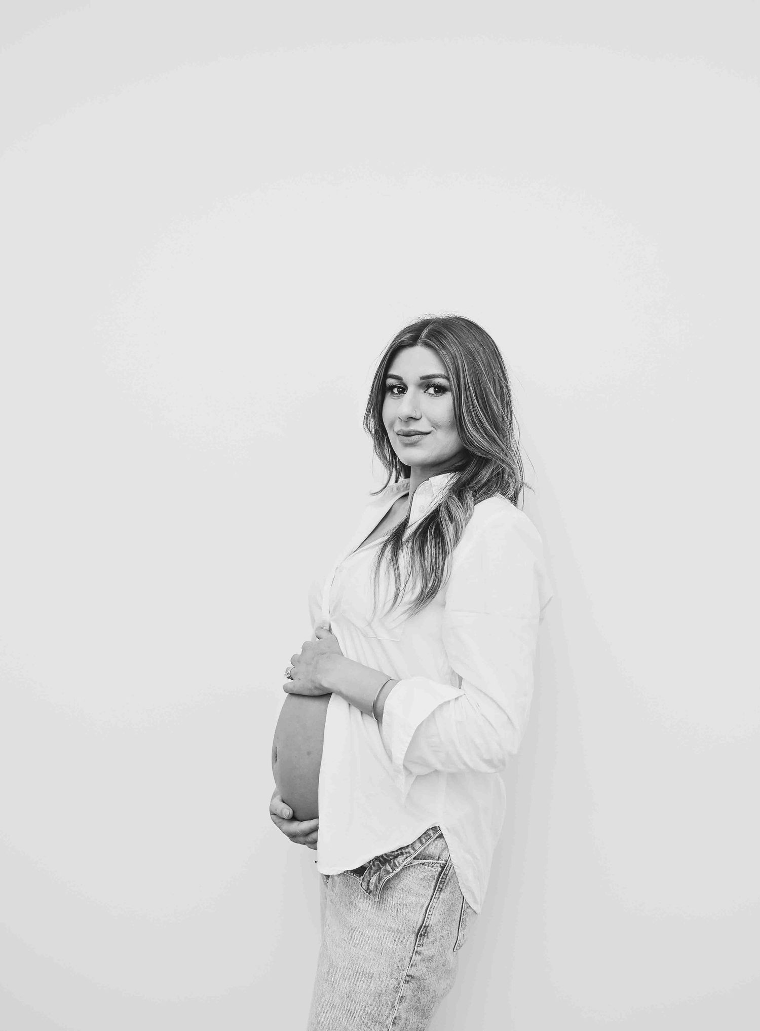 Black and white maternity portrait of a pregnant woman in white shirt cradling her baby bump.