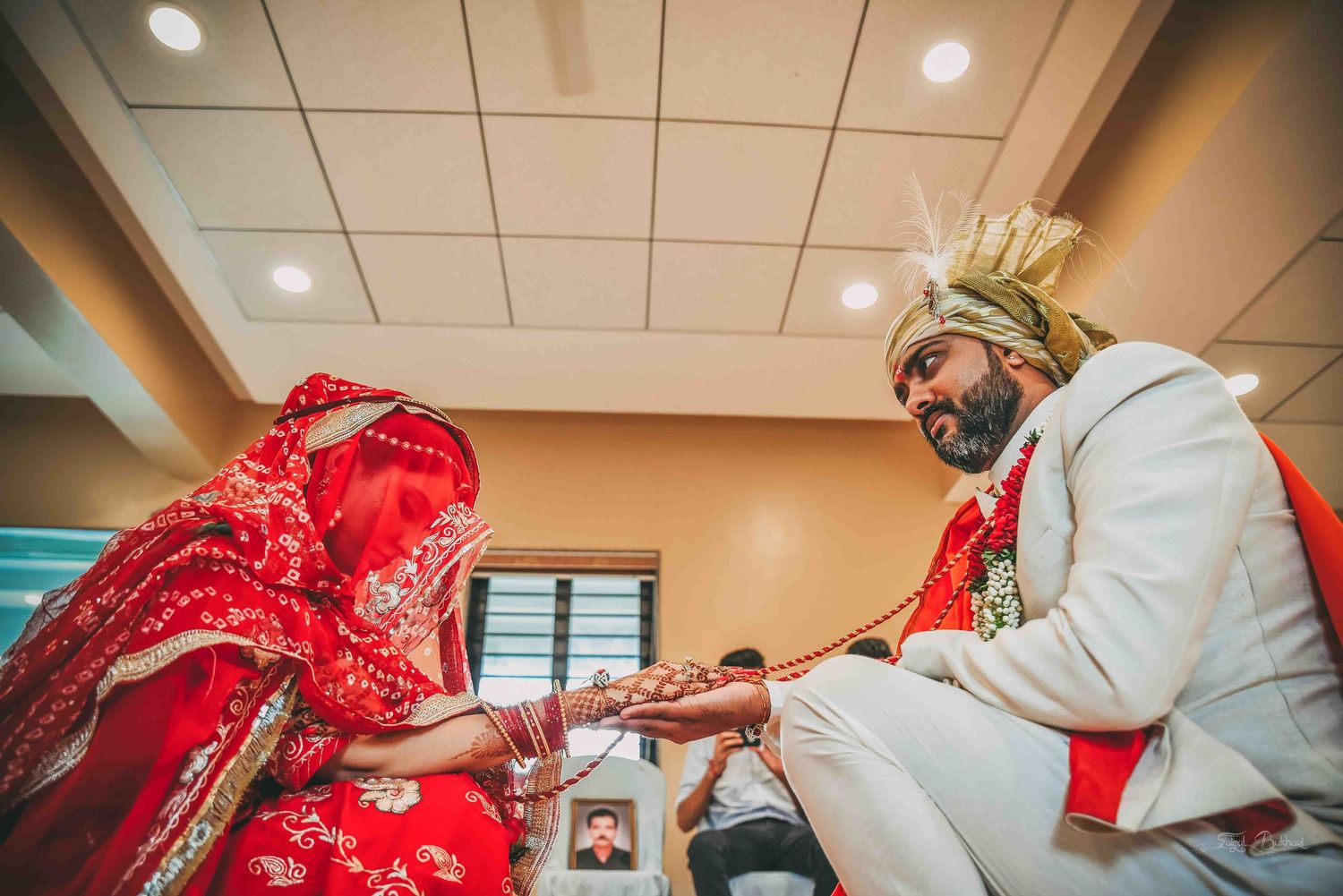 Indian bride in red lehenga and groom in white sherwani exchange garlands during traditional wedding ceremony.