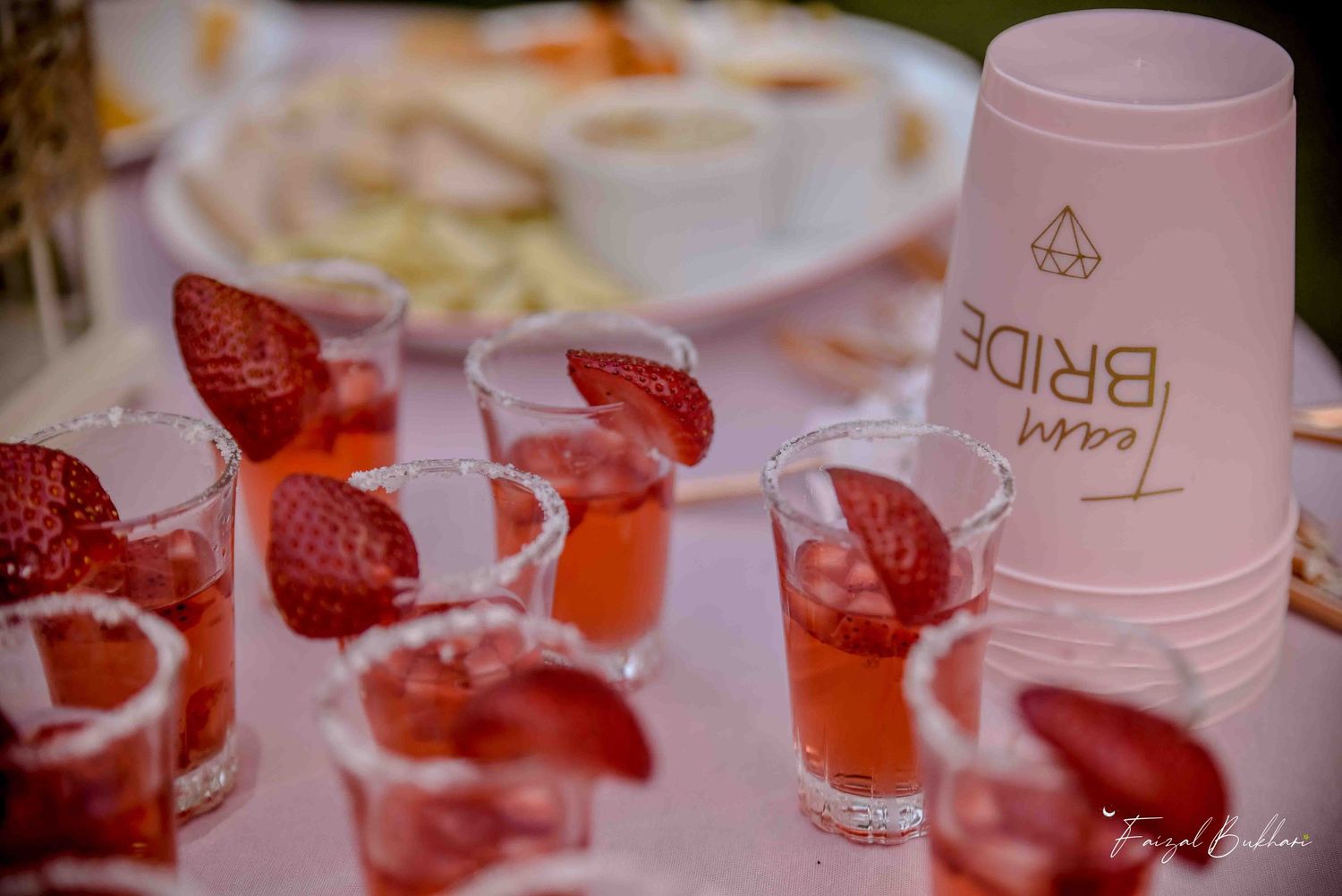 Strawberry garnished pink cocktail shots with Team Bride cups at bridal party table.