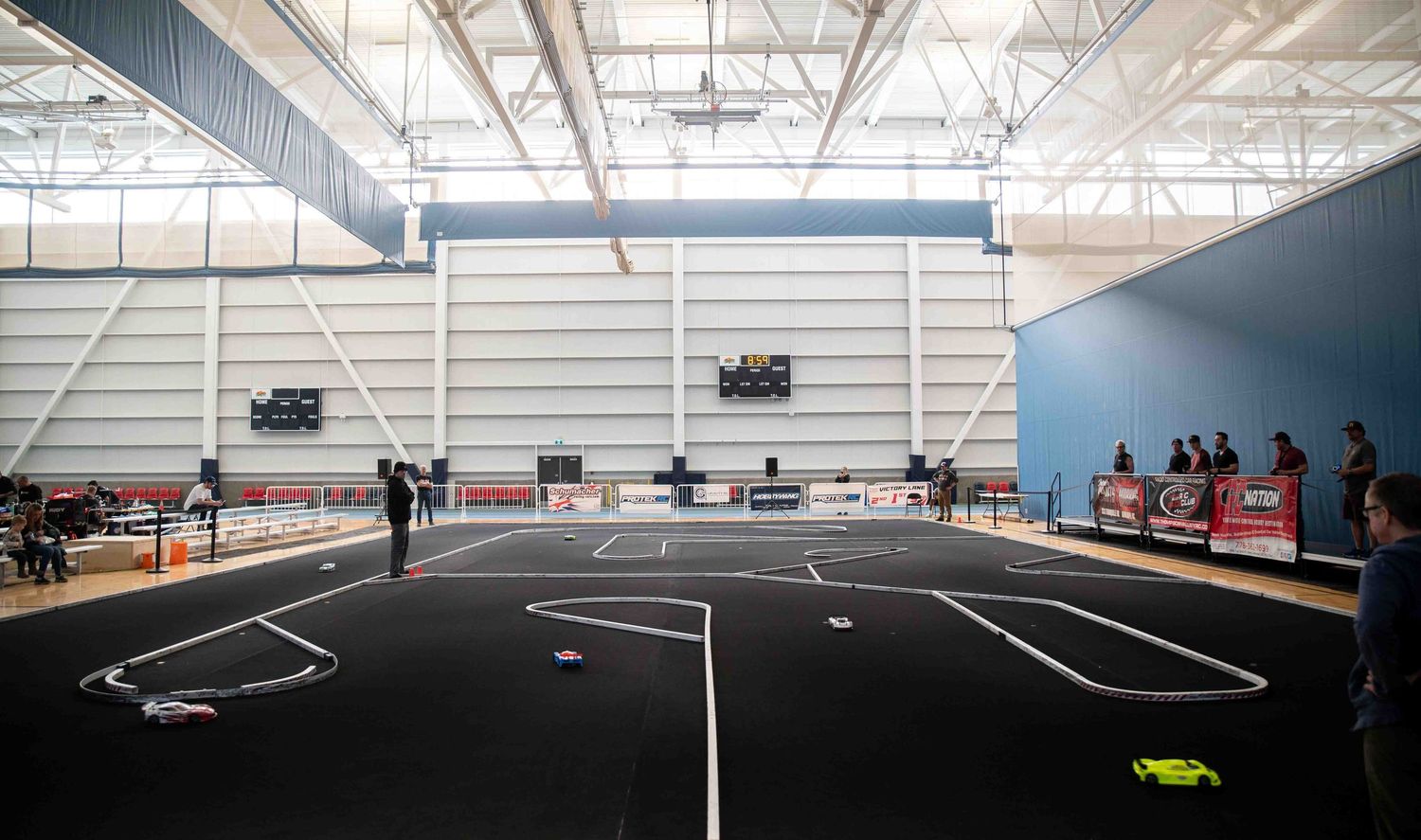 Wide-angle view of an indoor RC car racing track with white boundary lines in a large sports arena.