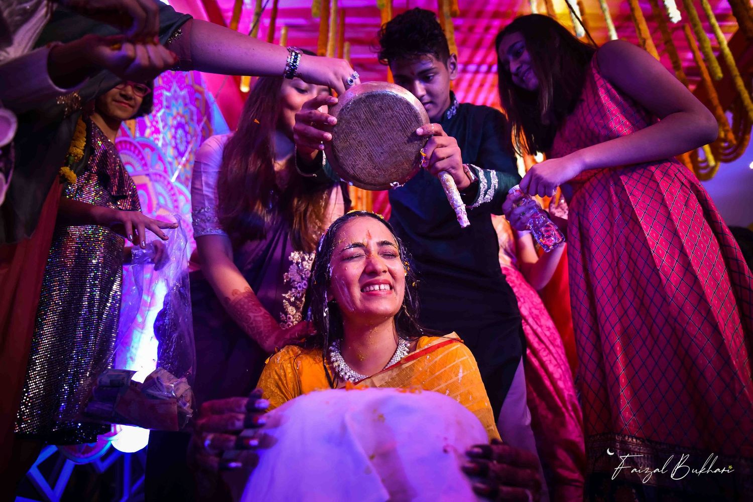 Joyful Indian bride laughing during haldi ceremony surrounded by family holding traditional items.
