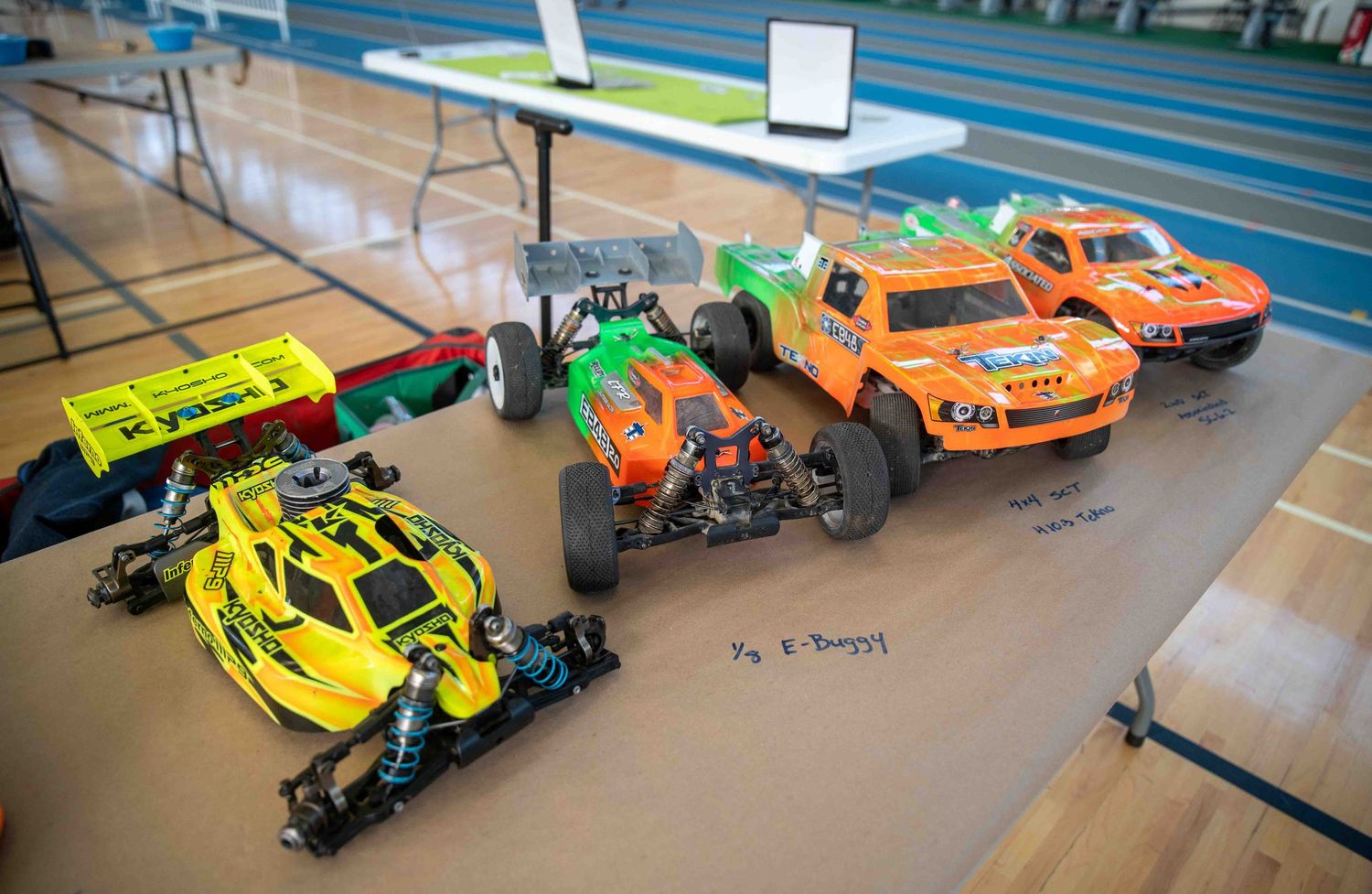 Colorful RC cars displayed on table at indoor hobby racing event.