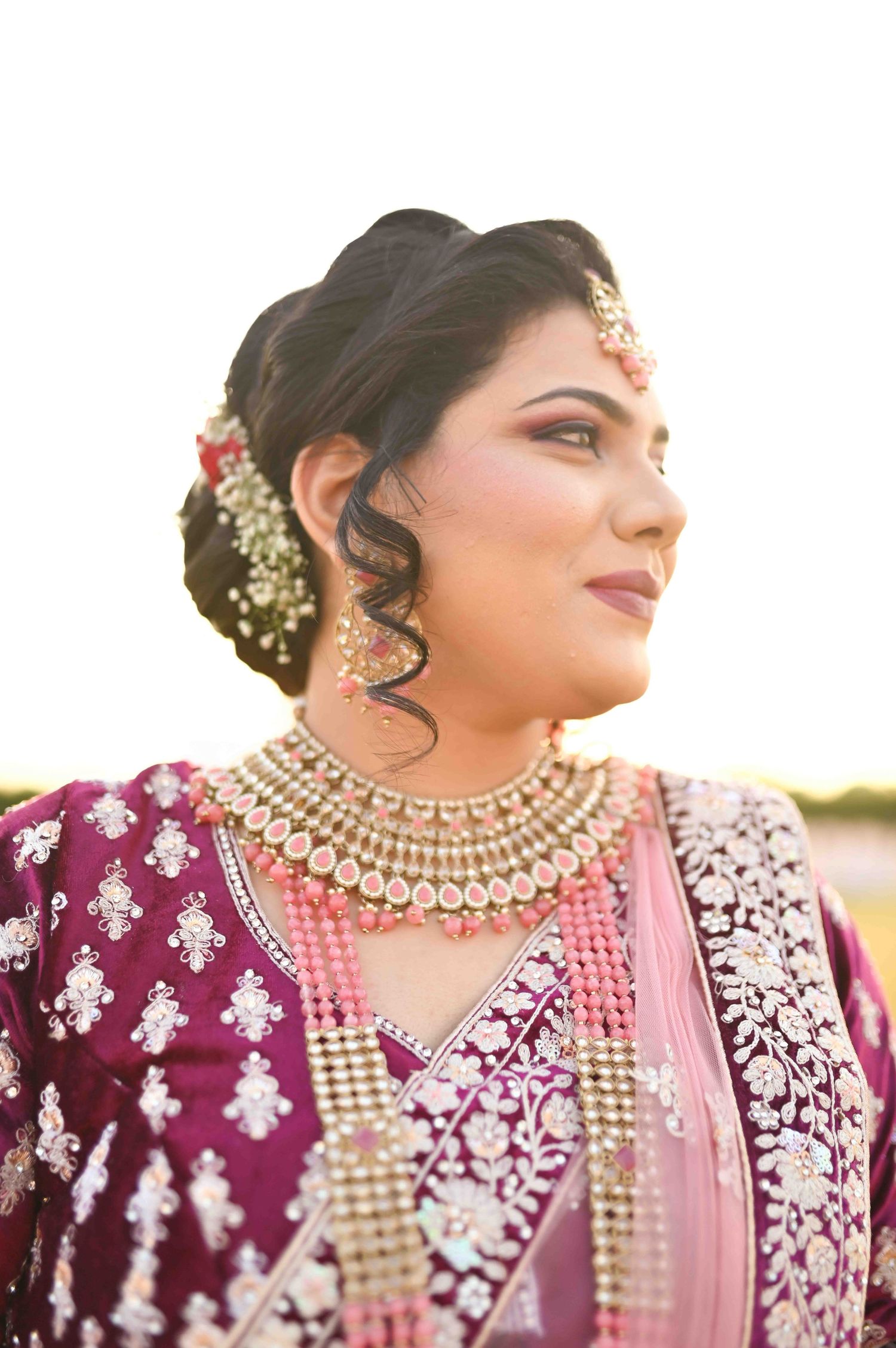 Indian bride in magenta lehenga wearing kundan necklace and maang tikka in golden light.