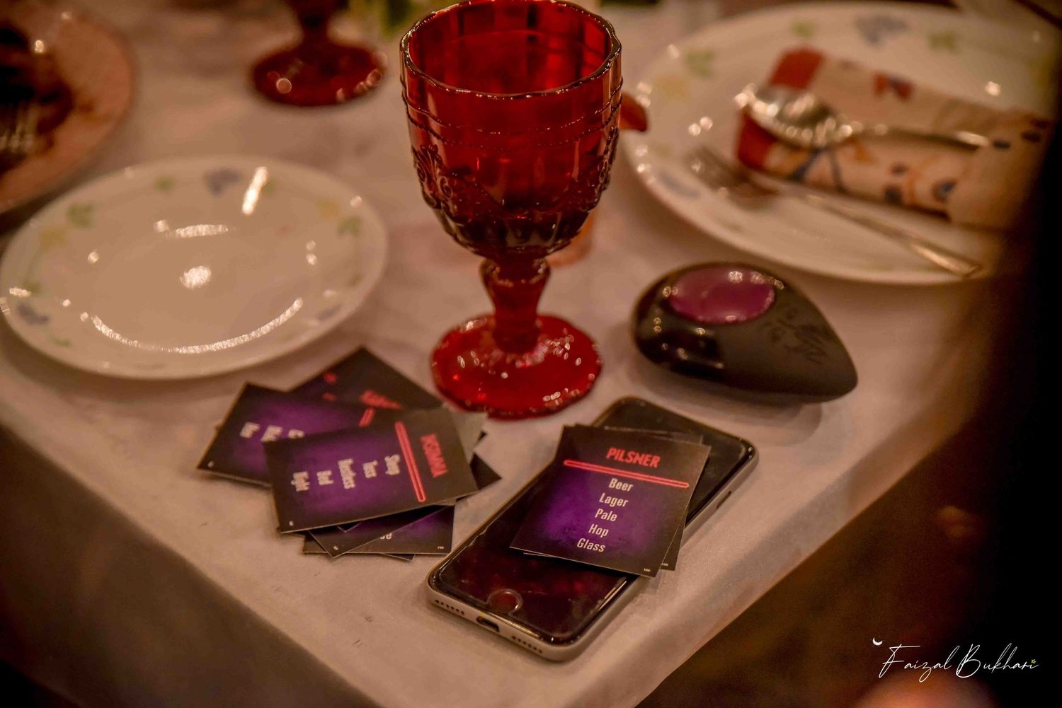 Red goblet and smartphone on white tablecloth at elegant dinner setting.